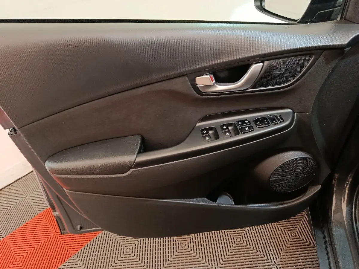Vue intérieure du panneau de porte côté conducteur d'une Hyundai Kona 1.6 Hybrid 2023, avec commandes électriques et poignée argentée.