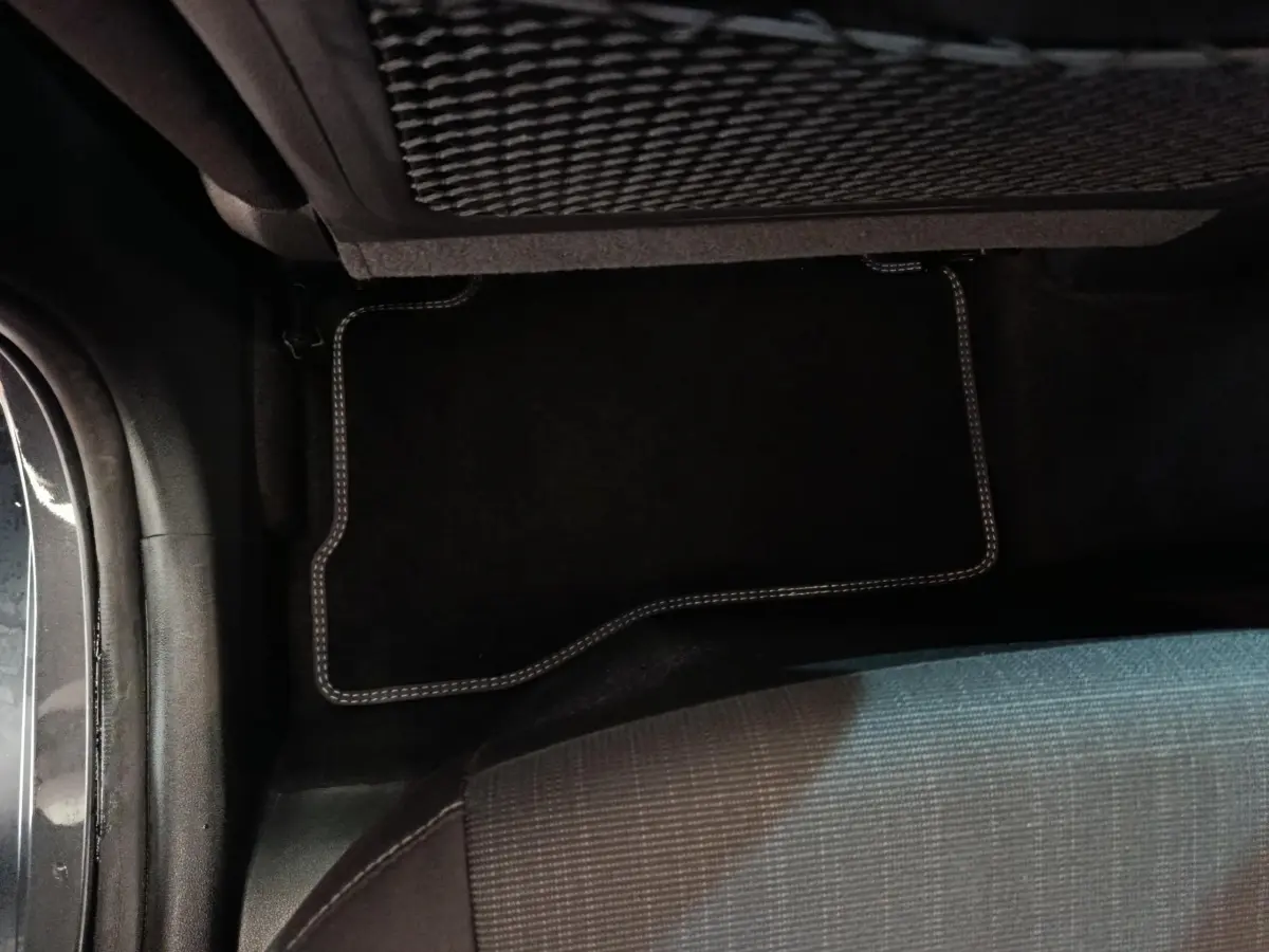 Vue intérieure du plancher arrière côté gauche d'un Hyundai Kona gris foncé avec tapis de sol noir à surpiqûres claires.