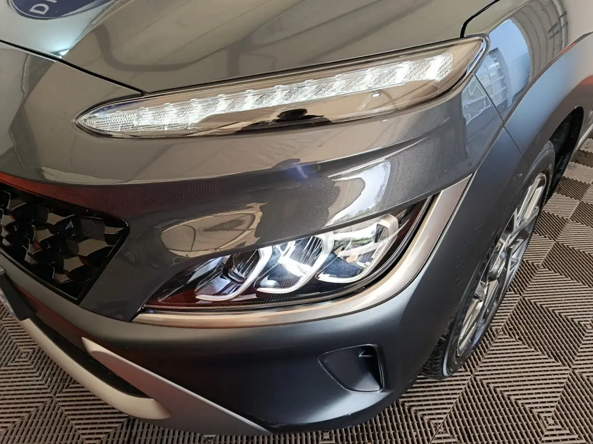 Gros plan sur le phare avant droit et la calandre d’un Hyundai Kona gris foncé 2023 avec feux LED et jante alliage.