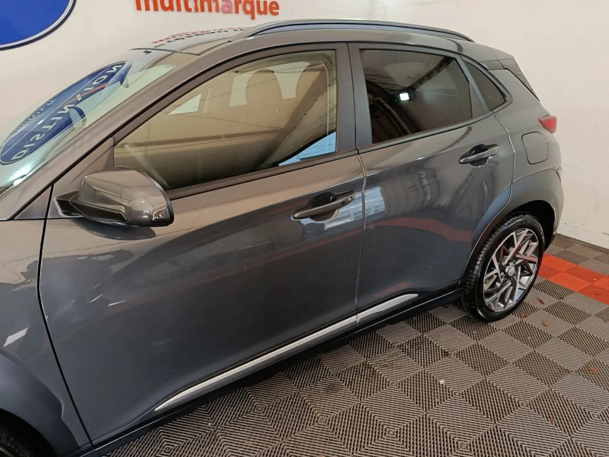 Vue de profil côté gauche d’un Hyundai Kona gris foncé 2023 avec jantes alliage et rétroviseur assorti.