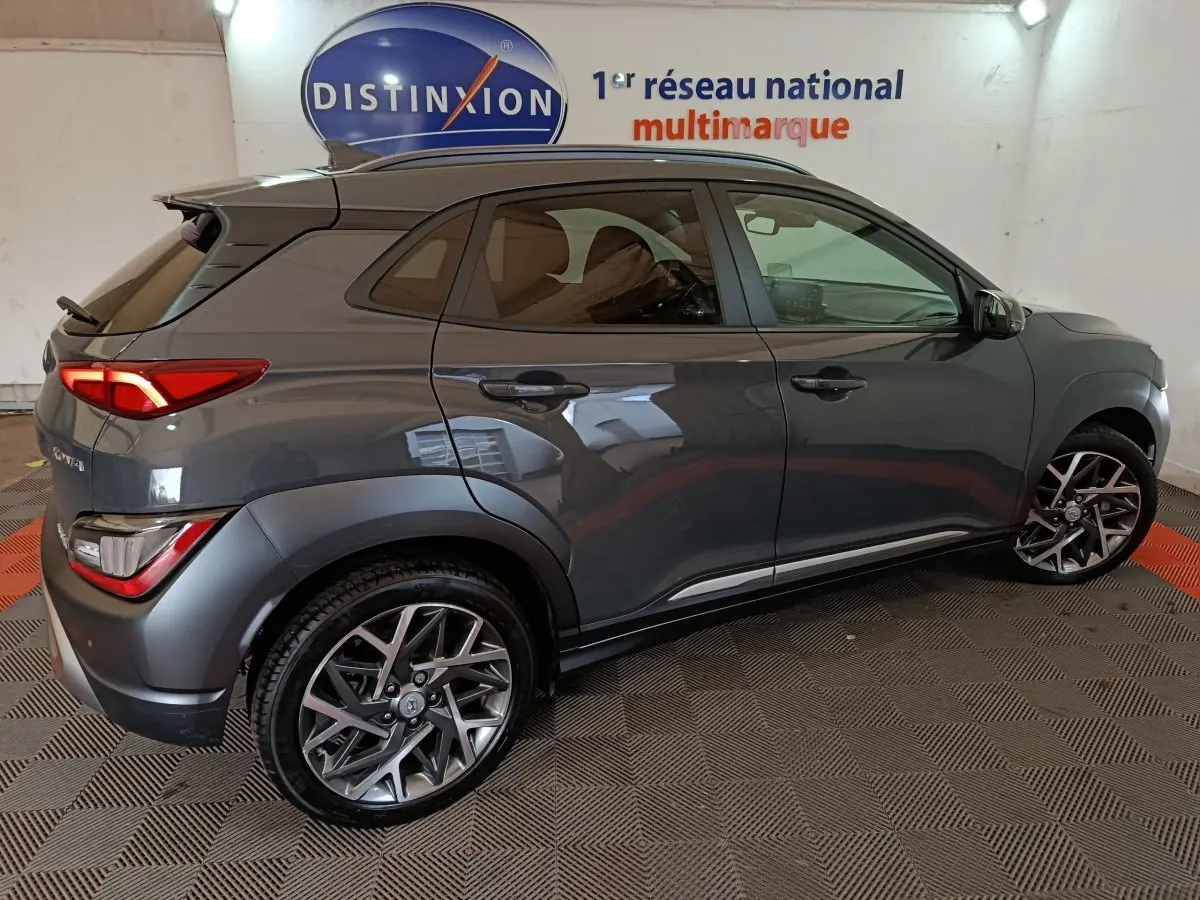 Vue côté droit d’un Hyundai Kona 1.6 Hybrid gris foncé, avec jantes alliage et feux arrière LED visibles en intérieur showroom.