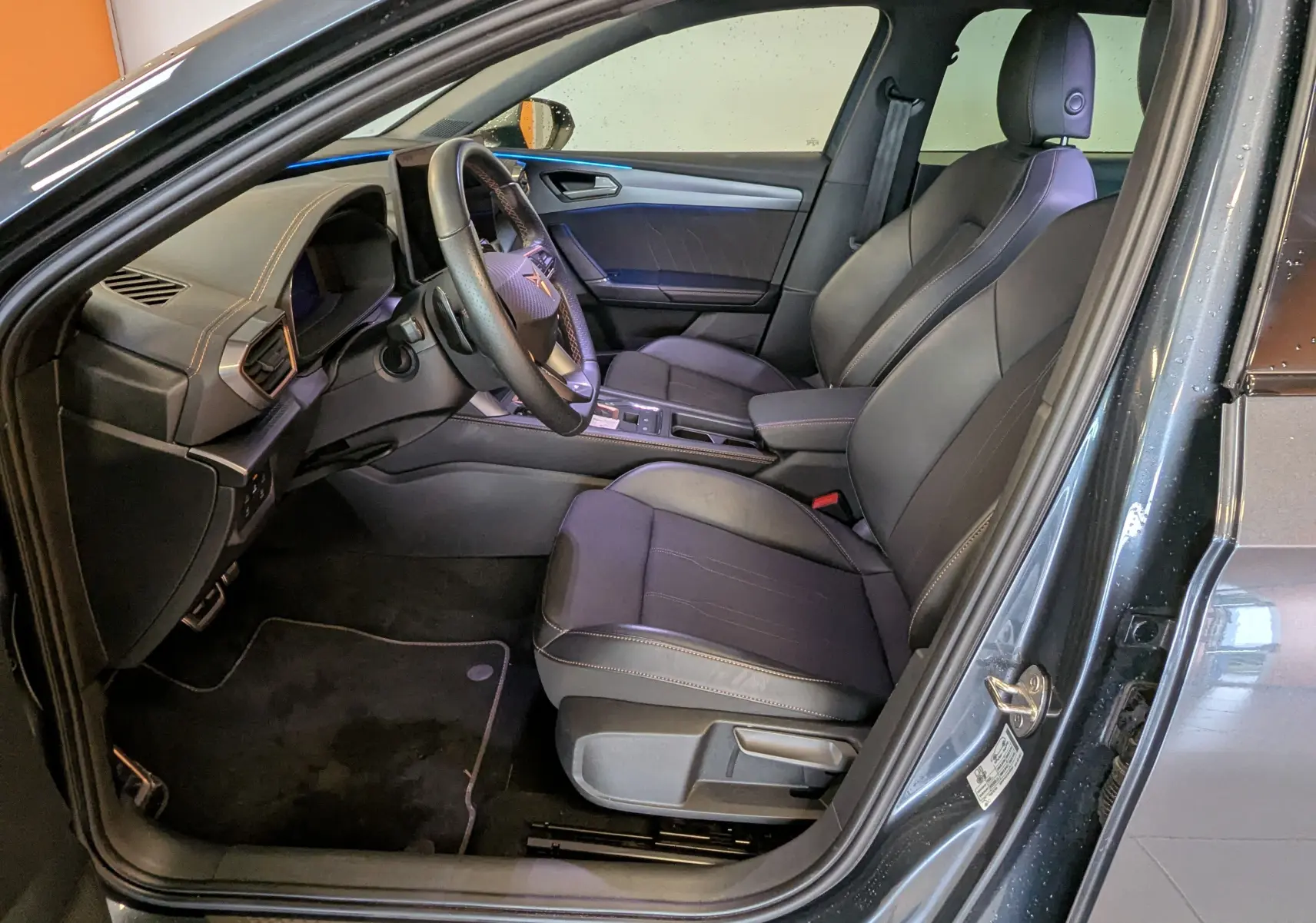 Vue intérieure côté conducteur de la CUPRA LEON ST gris magnetic, montrant sièges sport en cuir et volant multifonction.