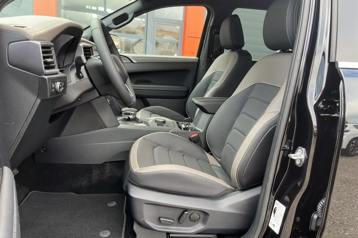 Vue intérieure côté conducteur du Volkswagen Amarok noir 2025, mettant en valeur les sièges cuir bi-ton et le volant multifonctions.
