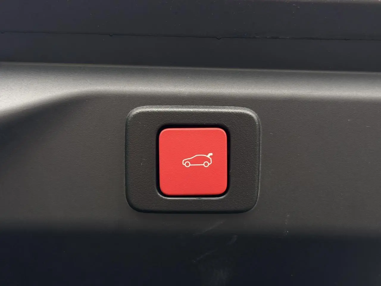 Bouton rouge d'ouverture électrique du hayon sur Peugeot 3008 Hybrid 145 e-DSC6 GT, intérieur coffre noir.