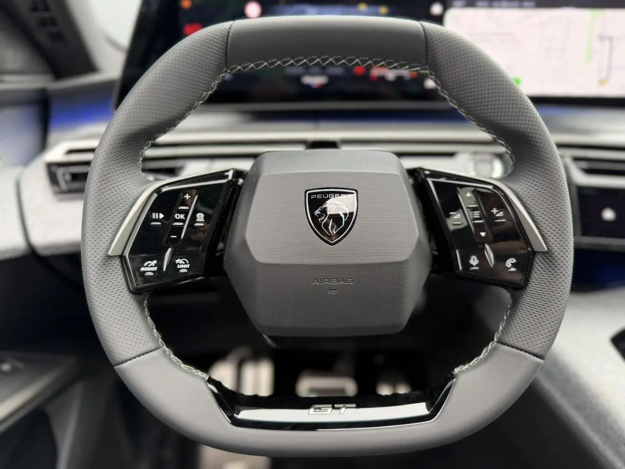 Volant compact cuir perforé gris avec badge GT au centre du tableau de bord du Peugeot 3008 Hybrid 2026.