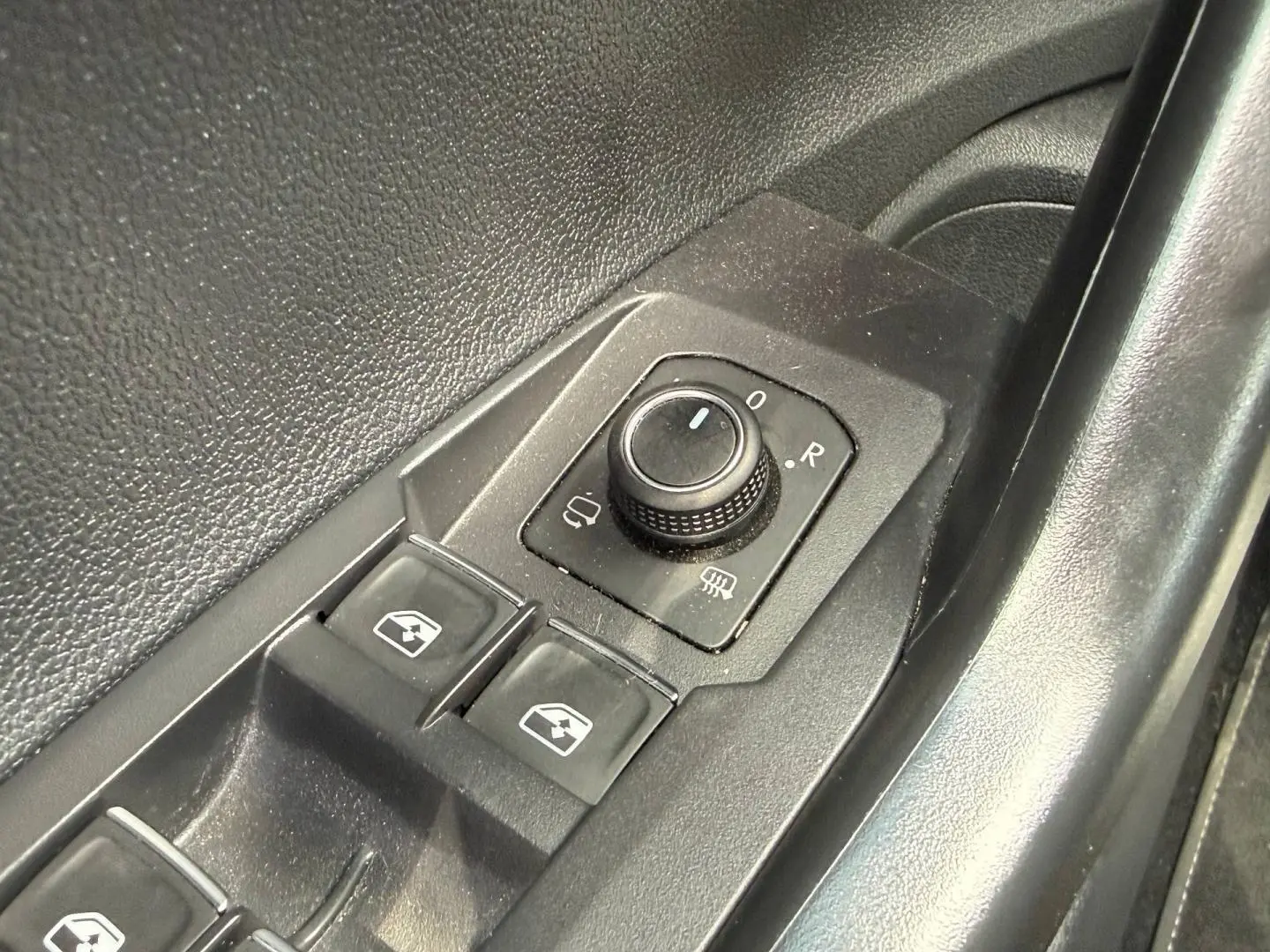 Gros plan sur les commandes de réglage des rétroviseurs et des vitres côté conducteur d’un Volkswagen Taigo gris.