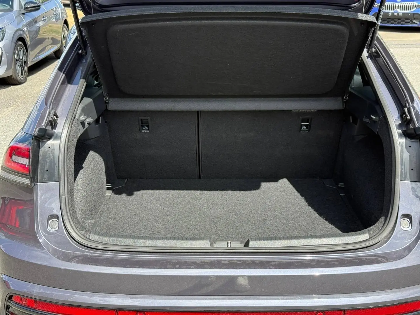 Coffre ouvert vu de l'arrière d'un Volkswagen Taigo gris 2025, montrant l'espace de chargement vide et la tablette cache-bagages relevée.