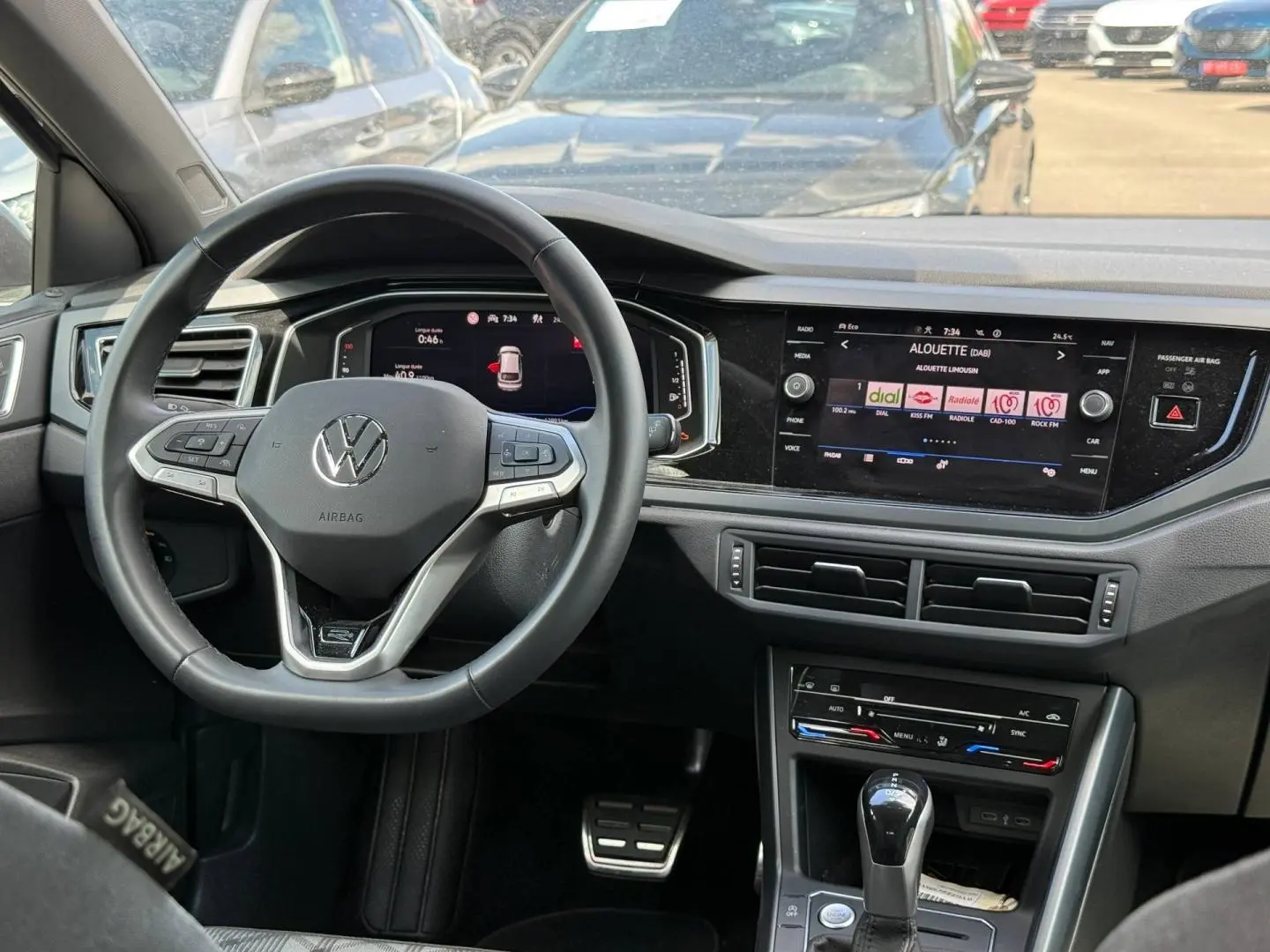 Vue intérieure du poste de conduite du Volkswagen Taigo gris, avec volant cuir multifonction et écran tactile central allumé.