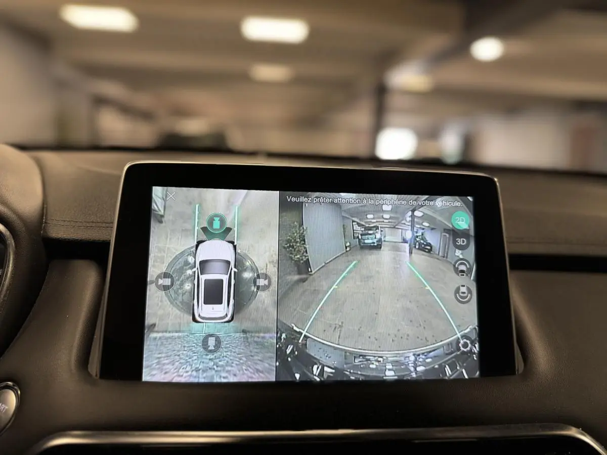 Écran tactile intérieur montrant la caméra 360° et vue arrière du MG MOTOR EHS noir en stationnement dans un garage.