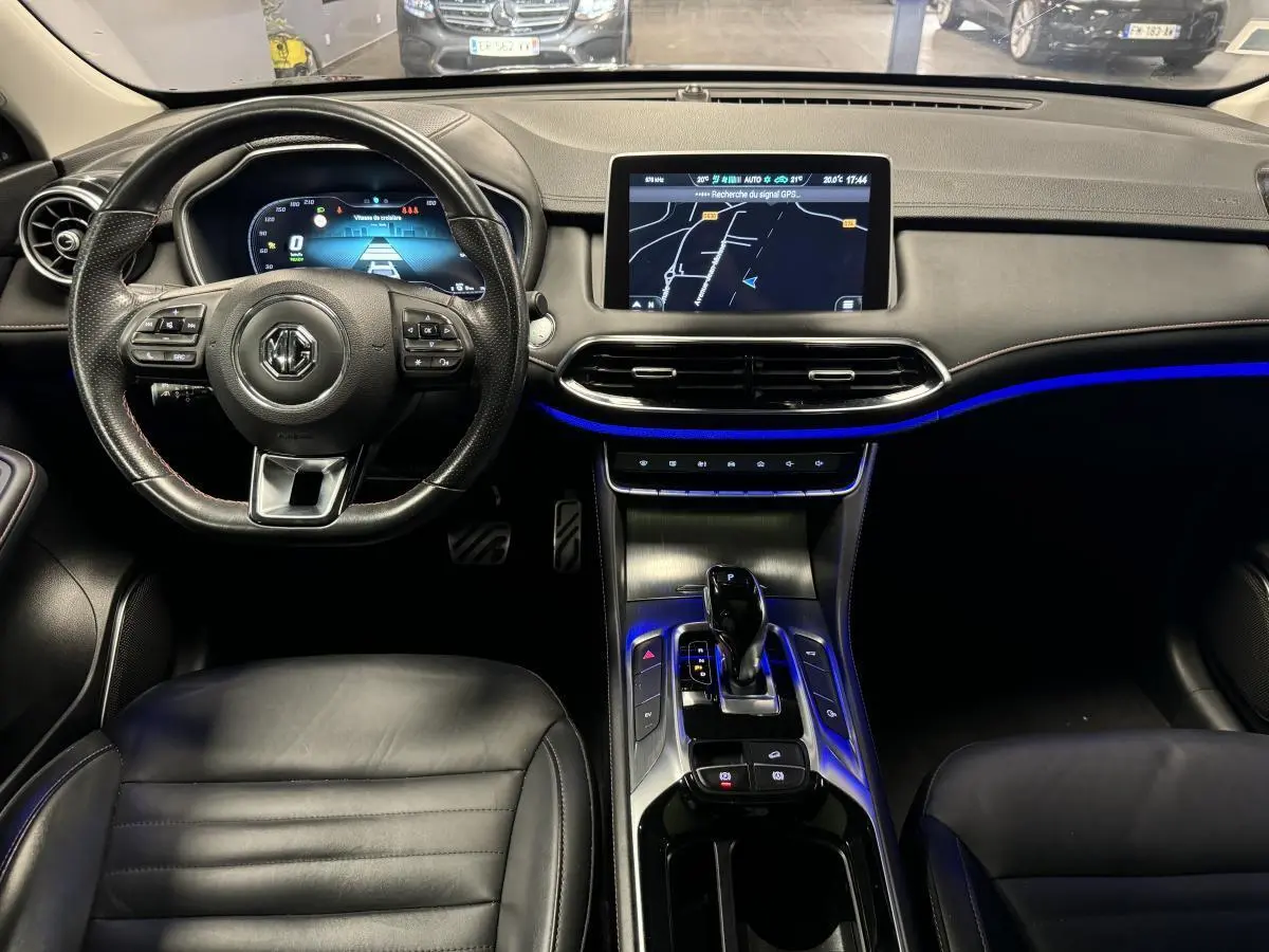 Vue intérieure avant du tableau de bord et console centrale du MG MOTOR EHS noir avec écran tactile et éclairage d'ambiance bleu.