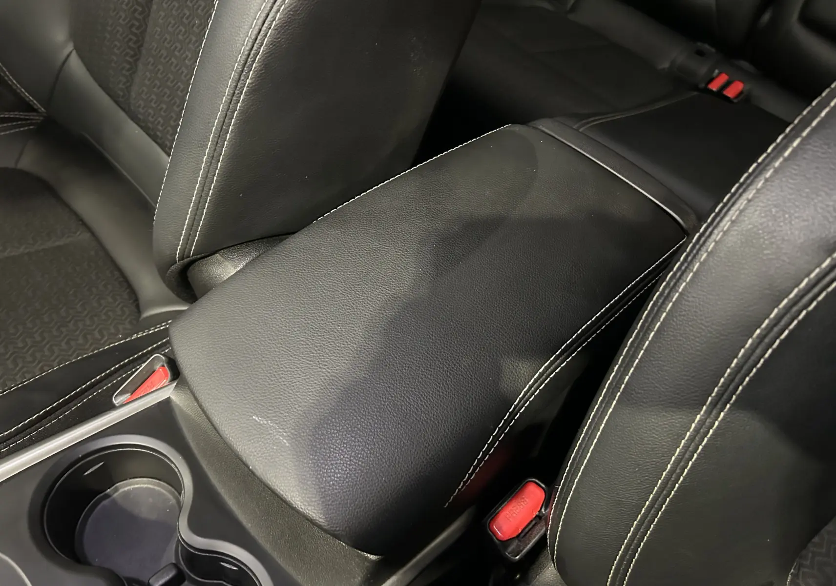 Gros plan sur l'accoudoir central en cuir noir avec surpiqûres blanches entre les sièges avant du Renault Kadjar bleu 2017.