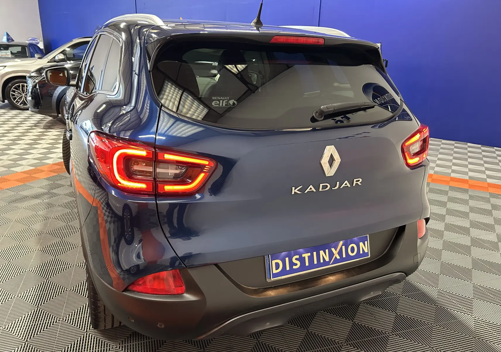 Vue 3/4 arrière droite d'un Renault Kadjar bleu 2017 avec feux arrière allumés dans un showroom.