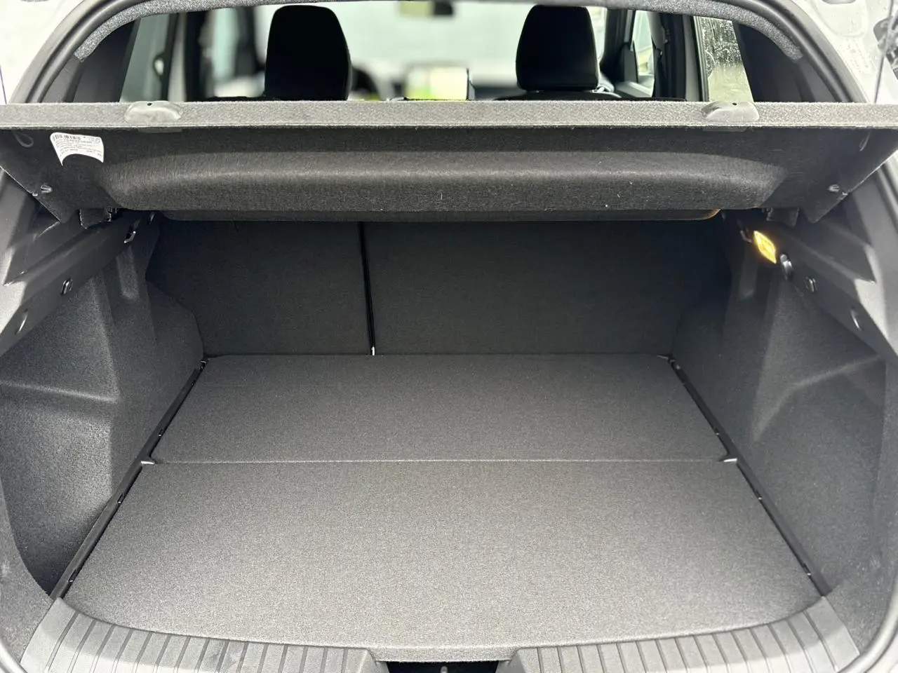 Coffre spacieux ouvert du Dacia Duster blanc Glacier 2025, montrant la banquette arrière rabattue et le revêtement noir.