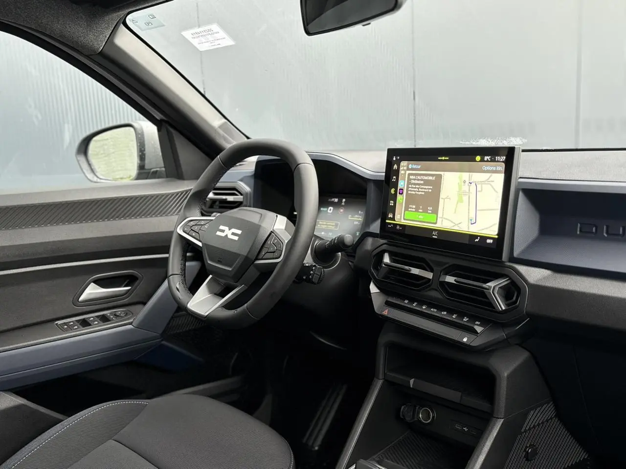 Intérieur du Dacia Duster 2025 côté conducteur, tableau de bord noir avec écran tactile GPS et volant multifonction.