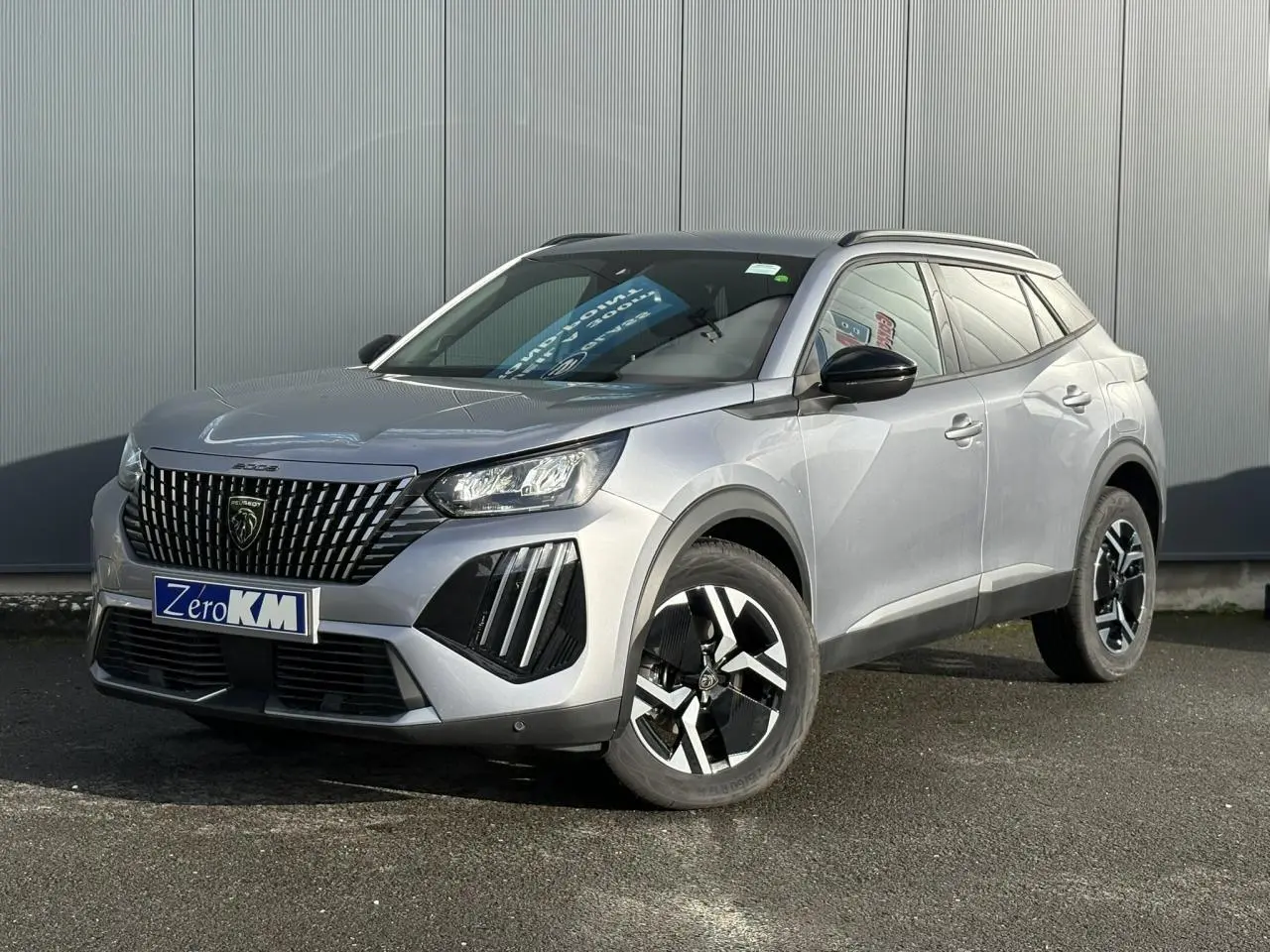 Peugeot 2008 Hybrid 145 Allure gris Artense en 3/4 avant droit, jantes bi-ton et toit noir brillant visible.