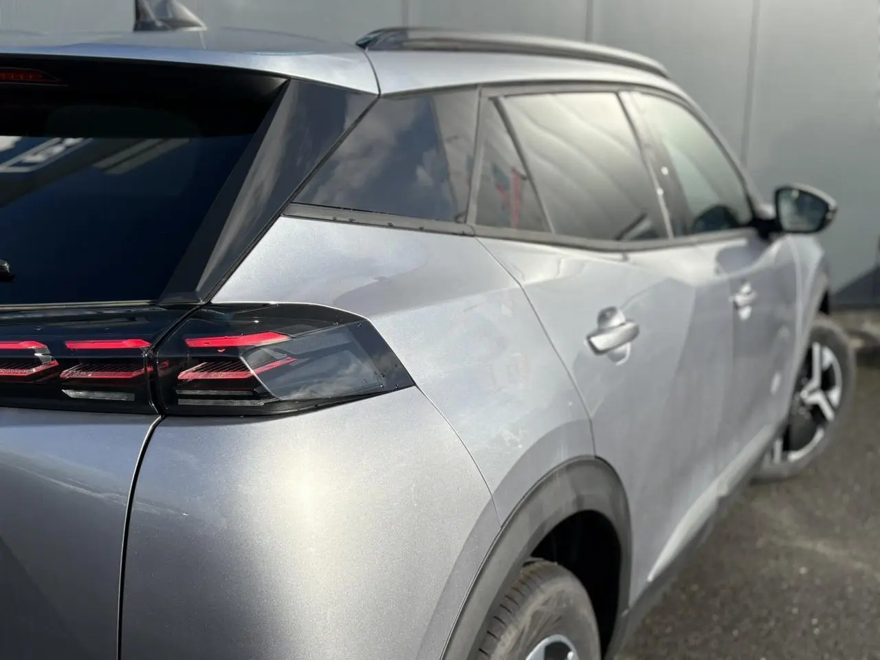 Vue 3/4 arrière droit d'un Peugeot 2008 Hybrid 145 gris Artense avec feux arrière LED 3 griffes et vitres surteintées.