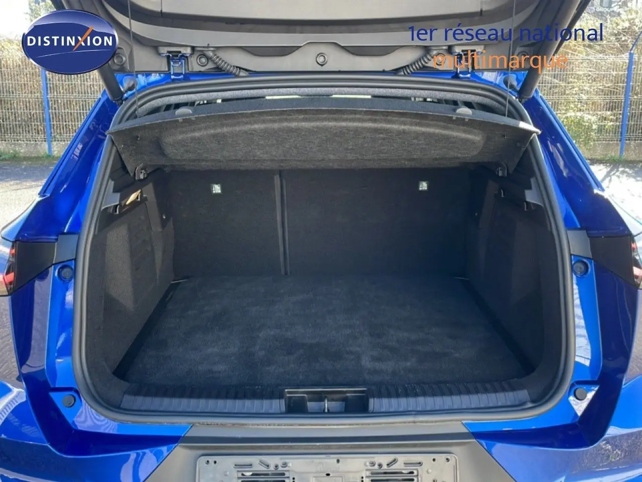 Coffre ouvert vu de l'arrière d'une Renault Symbioz bleu iron metal, montrant l'espace de chargement vide et la tablette cache-bagages.