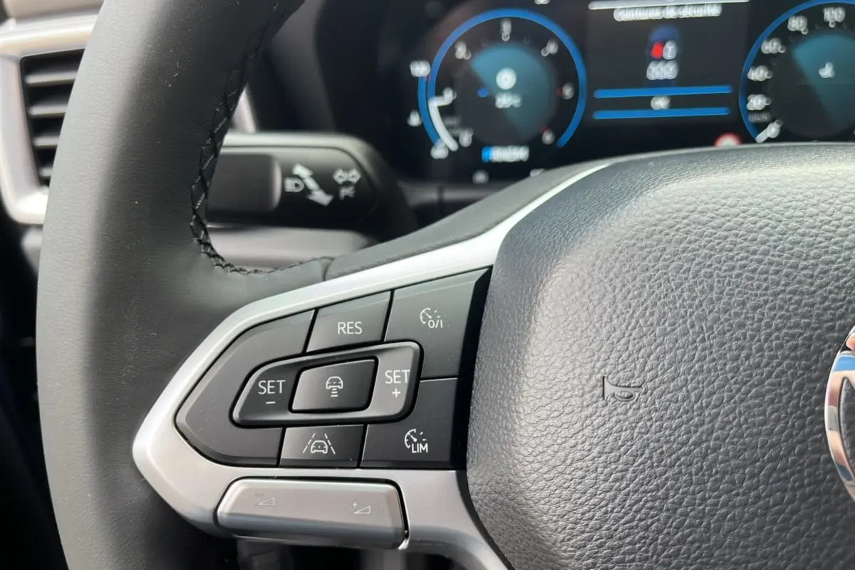 Gros plan sur le volant cuir noir du Volkswagen Amarok 2025 avec commandes multifonctions et tableau de bord digital flou.