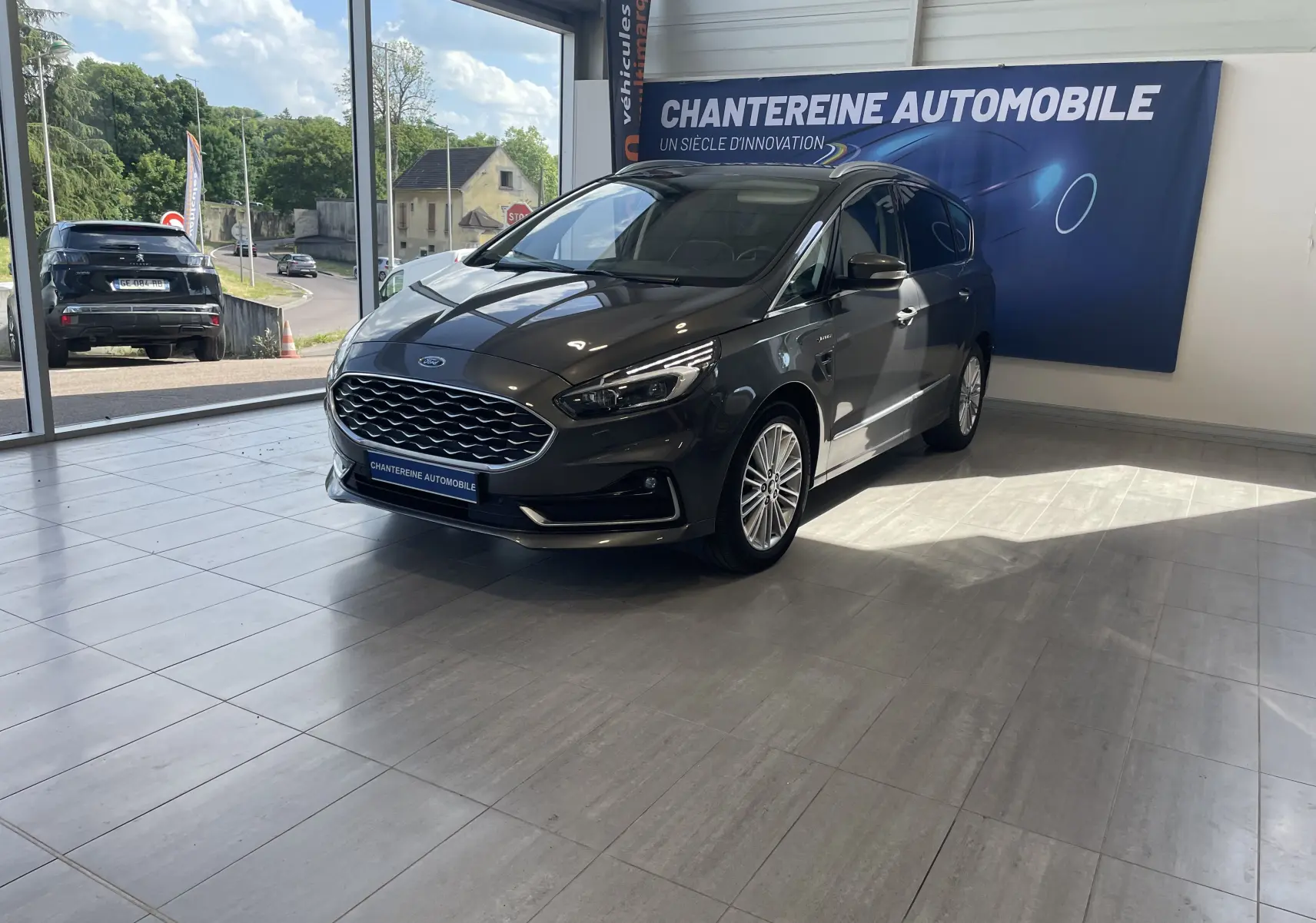 Ford S-MAX Vignale gris magnetic en 3/4 avant droit dans showroom avec bannière Chantreine Automobile.