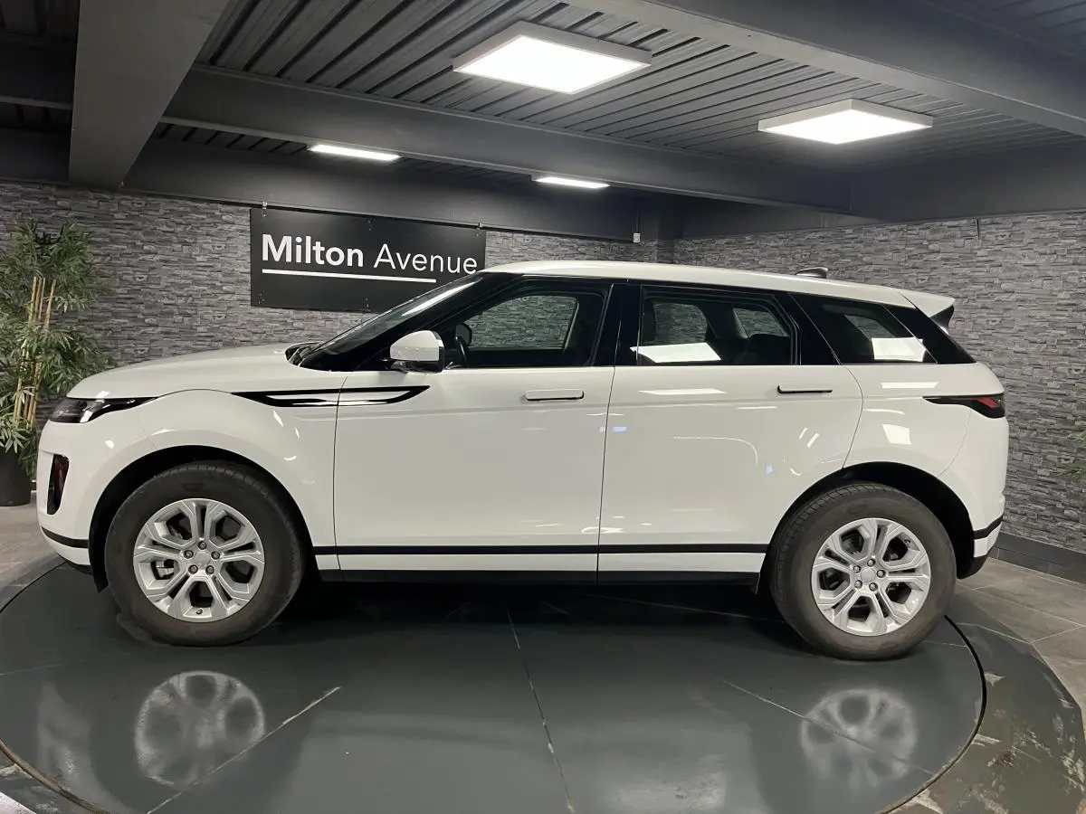 Range Rover Evoque blanc vu de profil côté gauche dans un showroom avec murs en pierre grise.