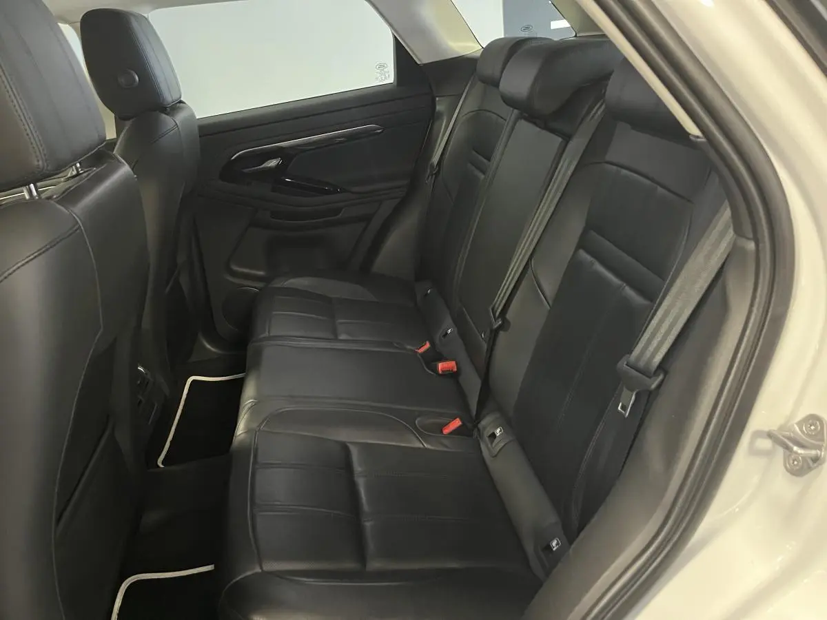Vue côté droit de l'habitacle arrière du Range Rover Evoque blanc, sièges cuir noir et ceintures visibles.