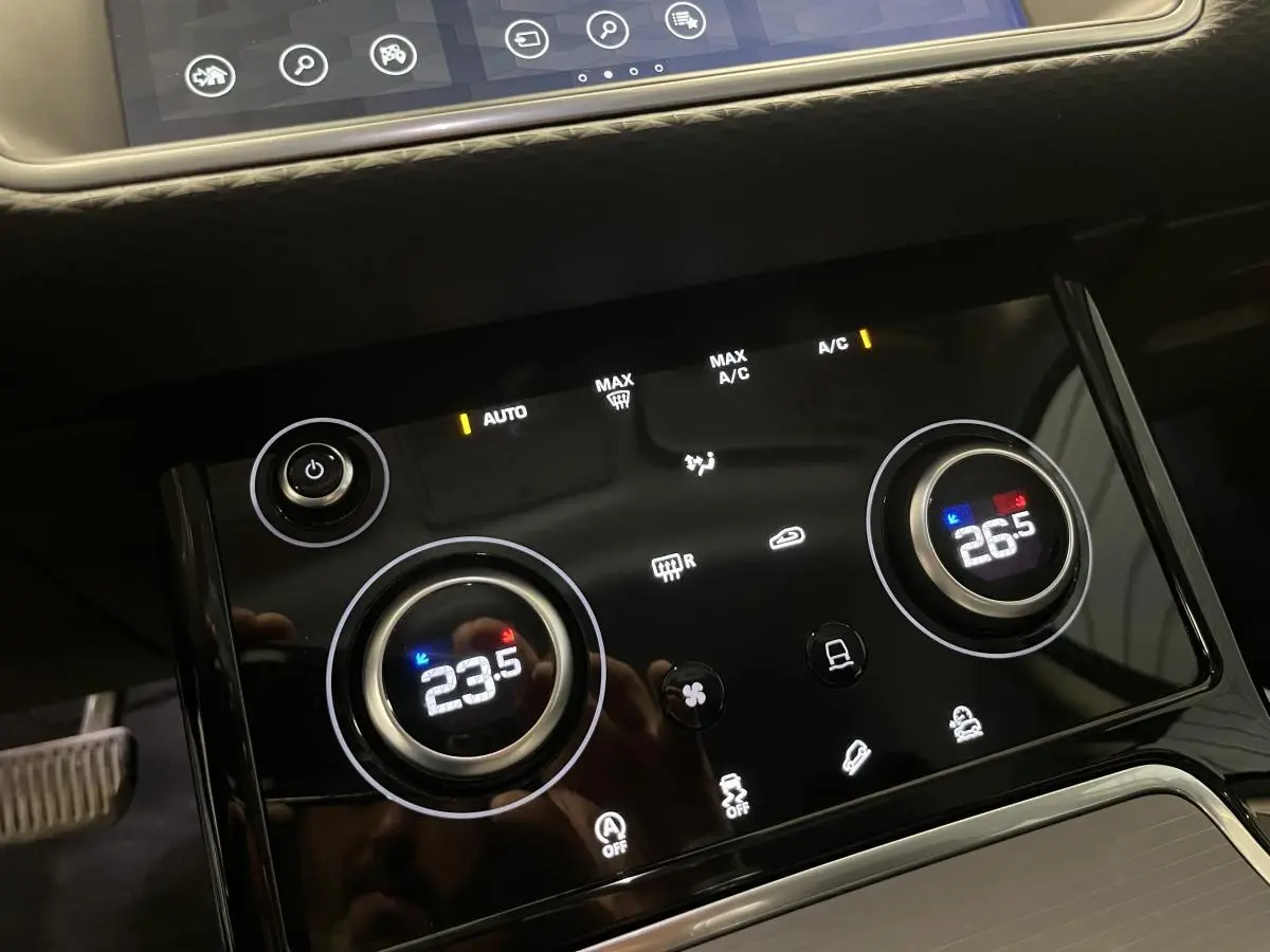 Panneau de commande de la climatisation bi-zone tactile du Range Rover Evoque blanc, affichant 23,5°C à gauche et 26,5°C à droite.