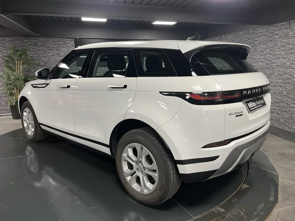 Vue 3/4 arrière droite d'un Range Rover Evoque blanc avec jantes 18 pouces et toit assorti en intérieur showroom.