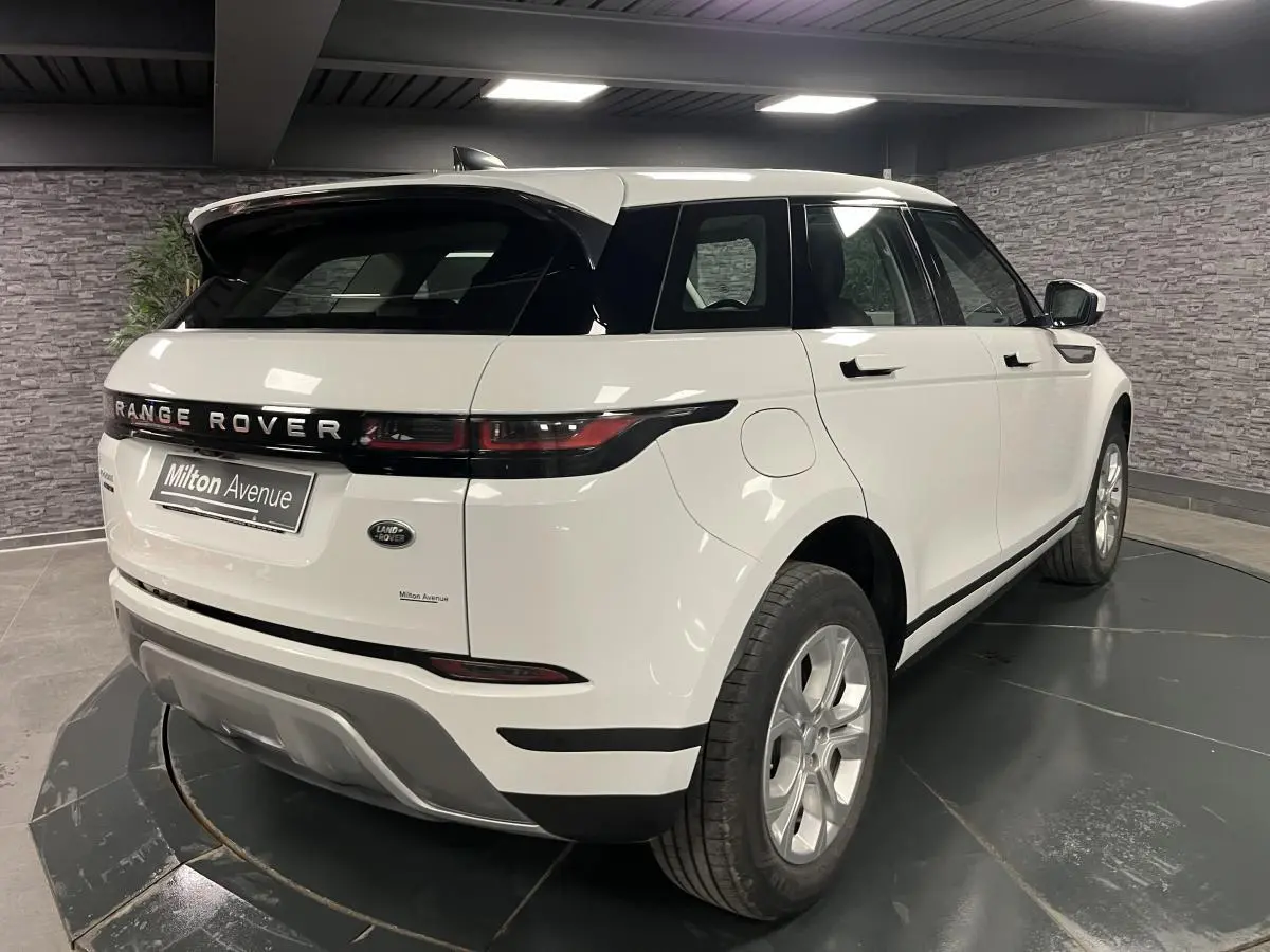 Vue 3/4 arrière droit d'un Range Rover Evoque blanc avec toit noir et jantes argentées en showroom.
