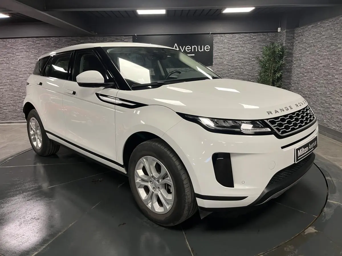 Range Rover Evoque blanc en 3/4 avant droit, avec calandre noire et jantes argentées dans un showroom.