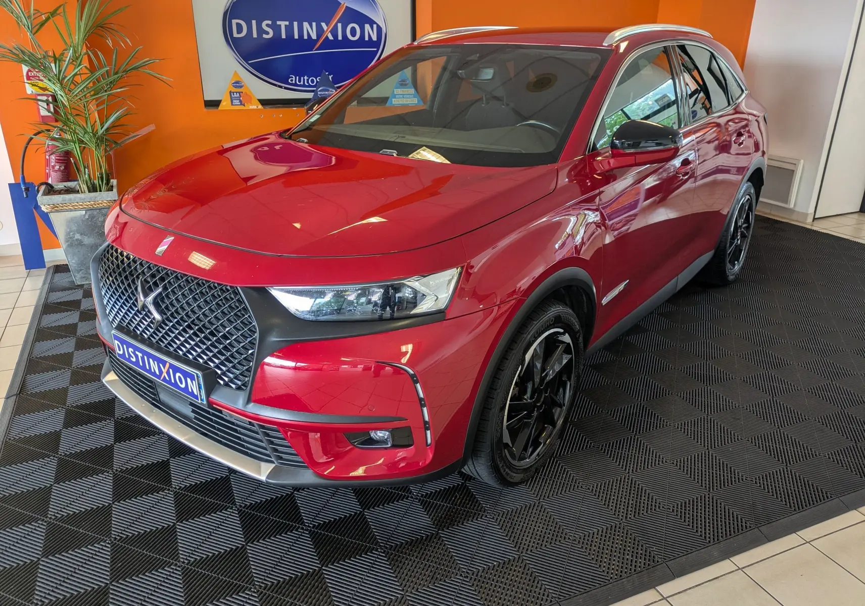 Vue 3/4 avant d’un DS7 rouge 2019 avec attelage, jantes noires et calandre distinctive dans un showroom.