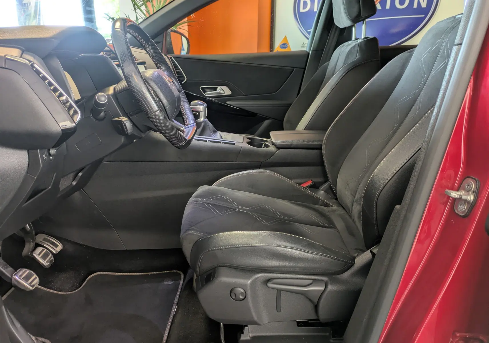 Vue intérieure côté conducteur du DS7 rouge 2019, montrant sièges en cuir noirs et volant avec boîte manuelle.