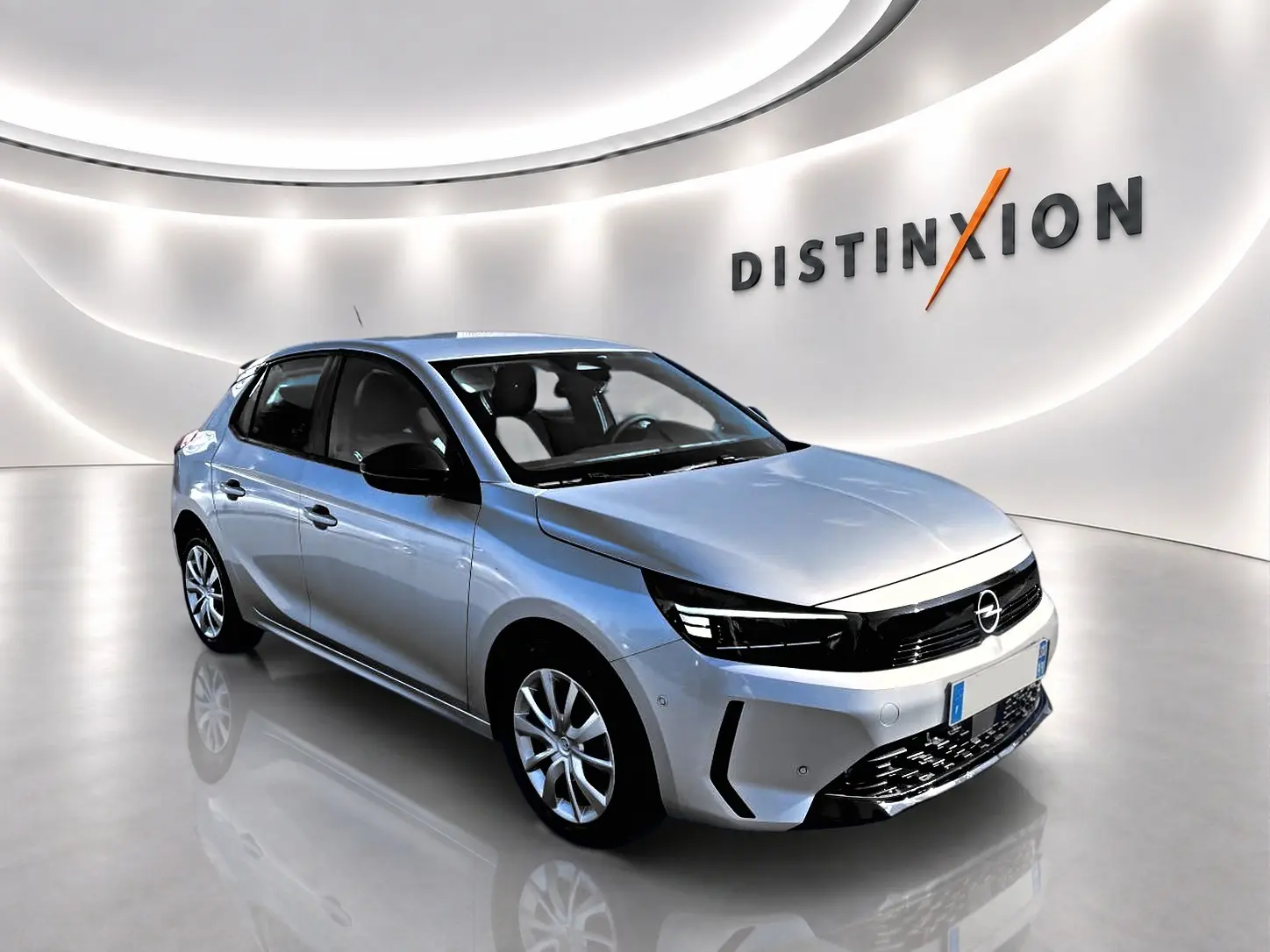 Opel Corsa gris alu vue 3/4 avant droit dans un showroom lumineux avec logo Distinxion en arrière-plan.