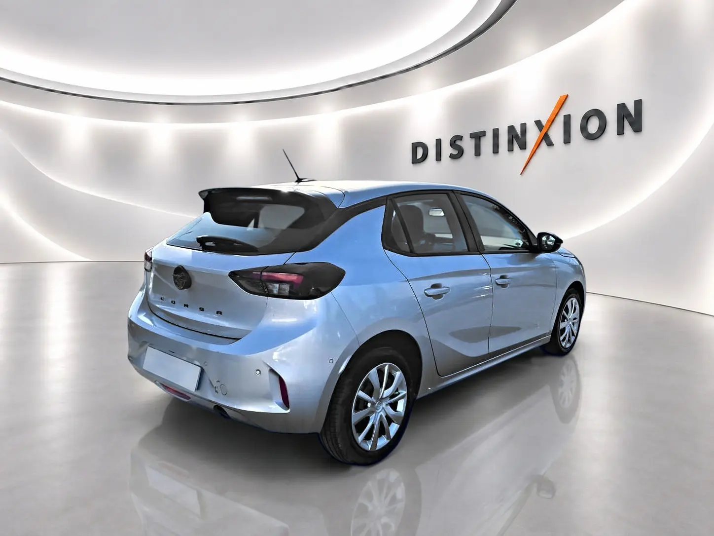 Opel Corsa gris alu vue 3/4 arrière droit en intérieur avec becquet et feux arrière foncés.