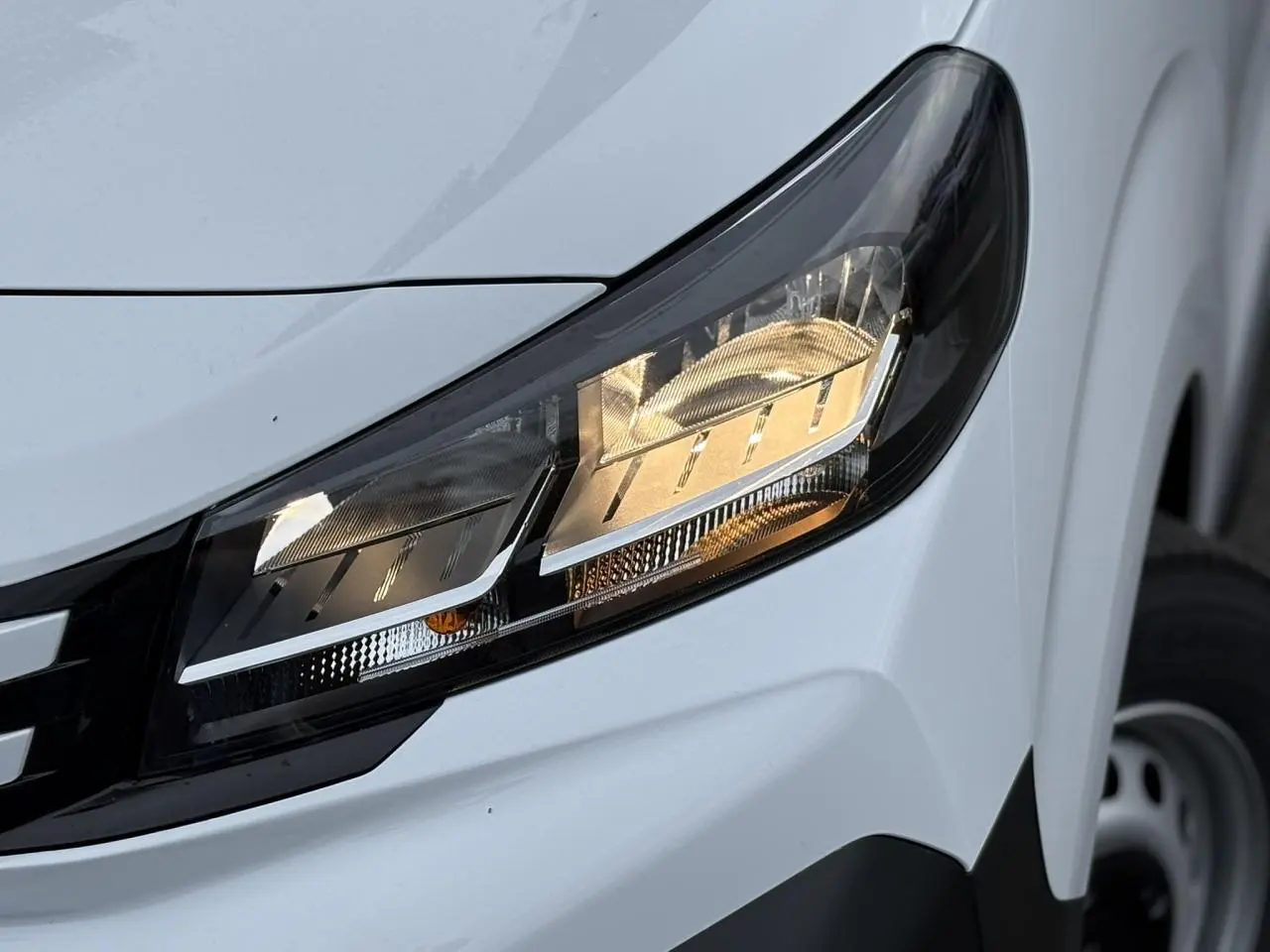 Gros plan sur le phare avant droit du Peugeot Expert Fourgon blanc Icy, avec partie de la roue en arrière-plan.