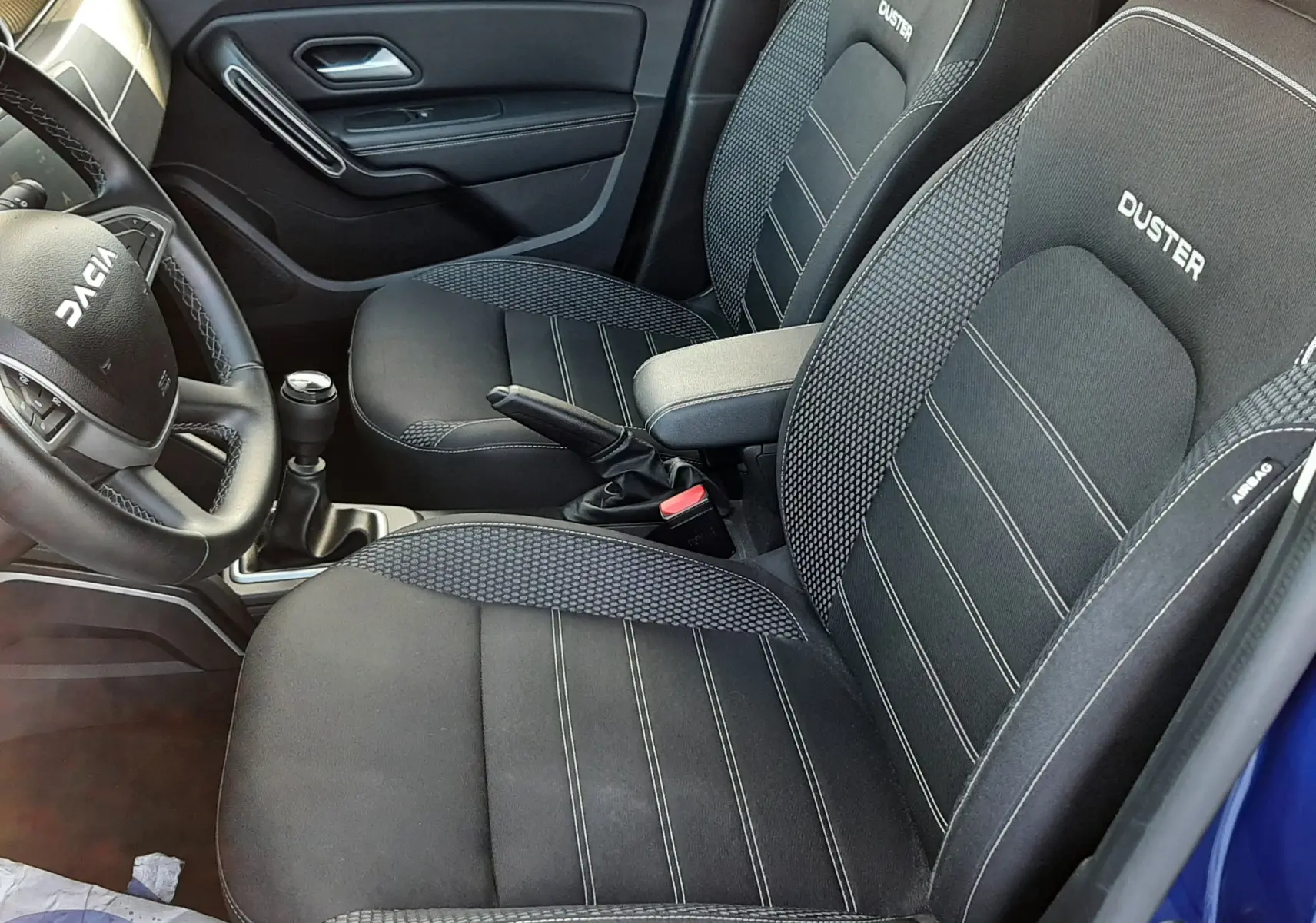 Vue intérieure côté conducteur du Dacia Duster bleu 2023, sièges noirs avec logo DUSTER brodé et volant multifonction.