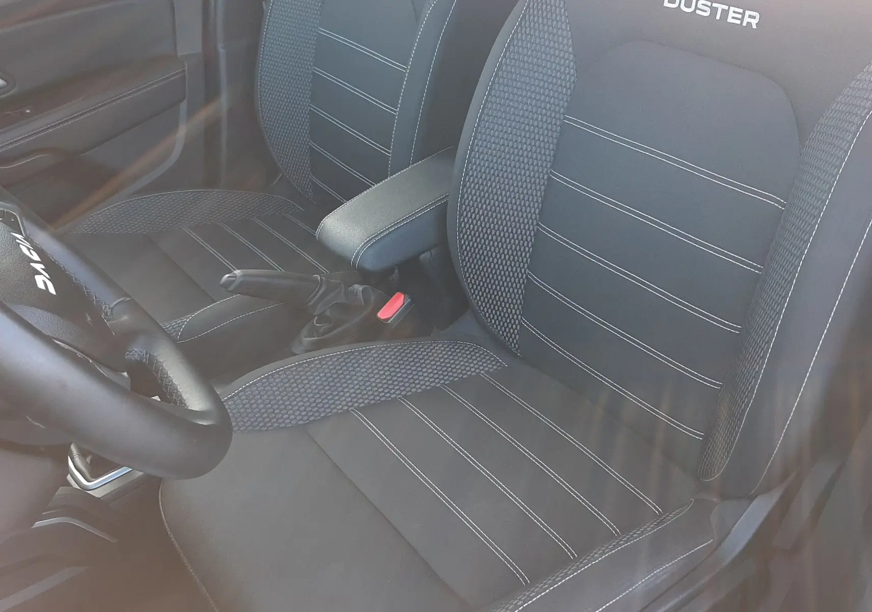 Vue intérieure en plongée des sièges avant noirs du Dacia Duster 2023 avec logo brodé et accoudoir central.