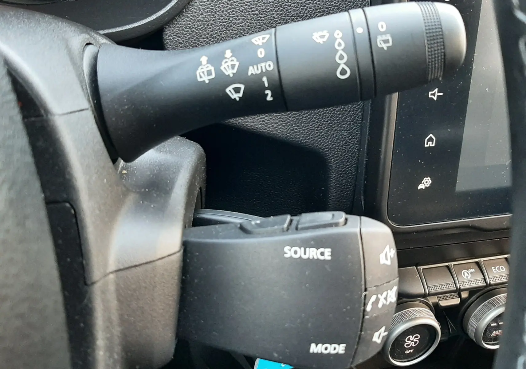 Gros plan sur les commandes au volant du Dacia Duster bleu 2023, avec levier d'essuie-glace et boutons audio visibles.