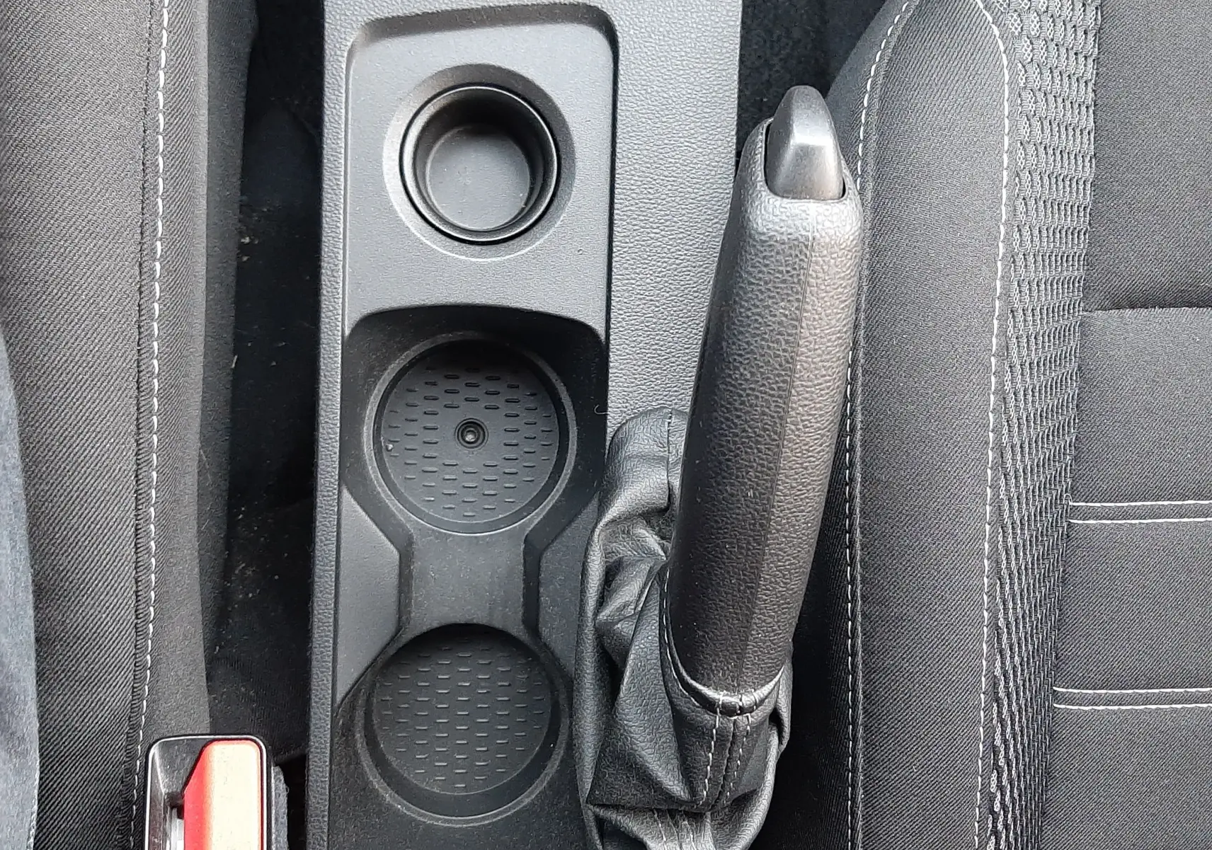 Vue plongeante sur la console centrale noire du Dacia Duster 2023, avec frein à main manuel et porte-gobelets.