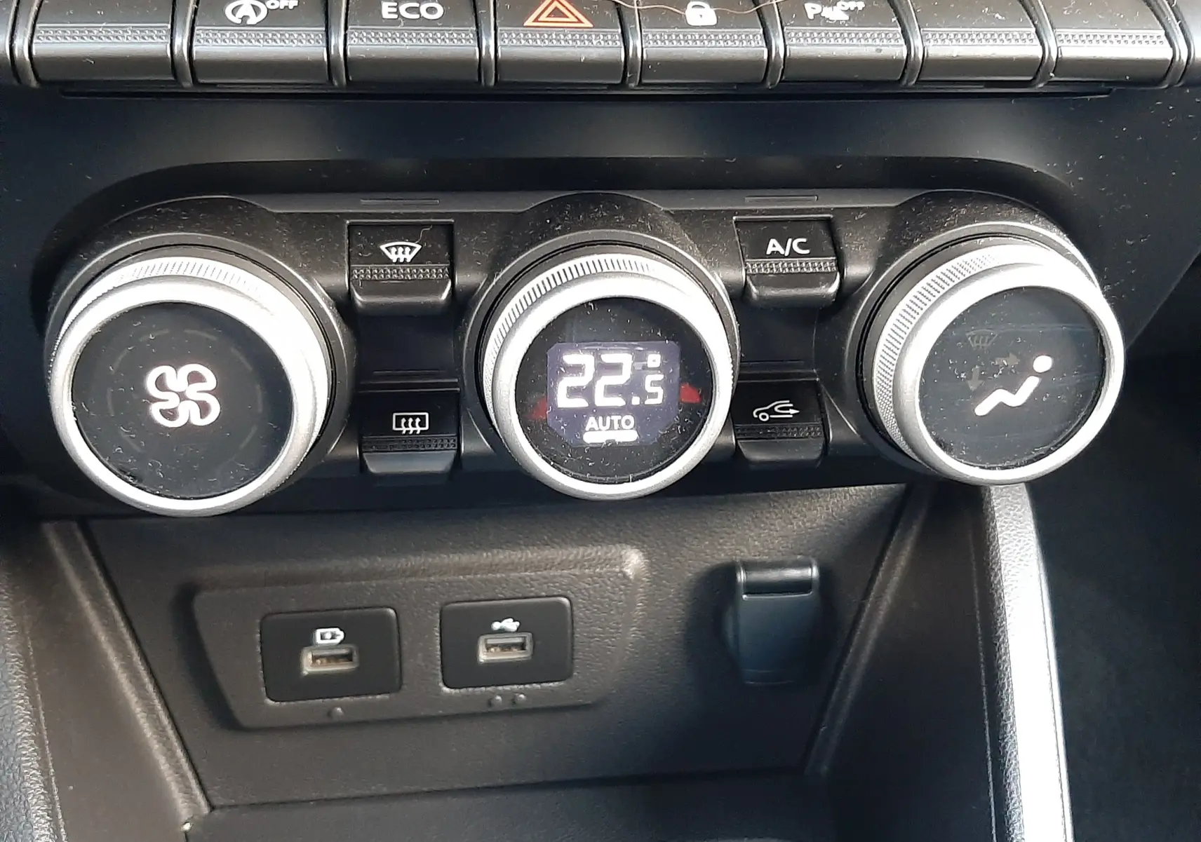 Vue rapprochée du tableau de bord du Dacia Duster bleu 2023, montrant les commandes de climatisation et les ports USB.
