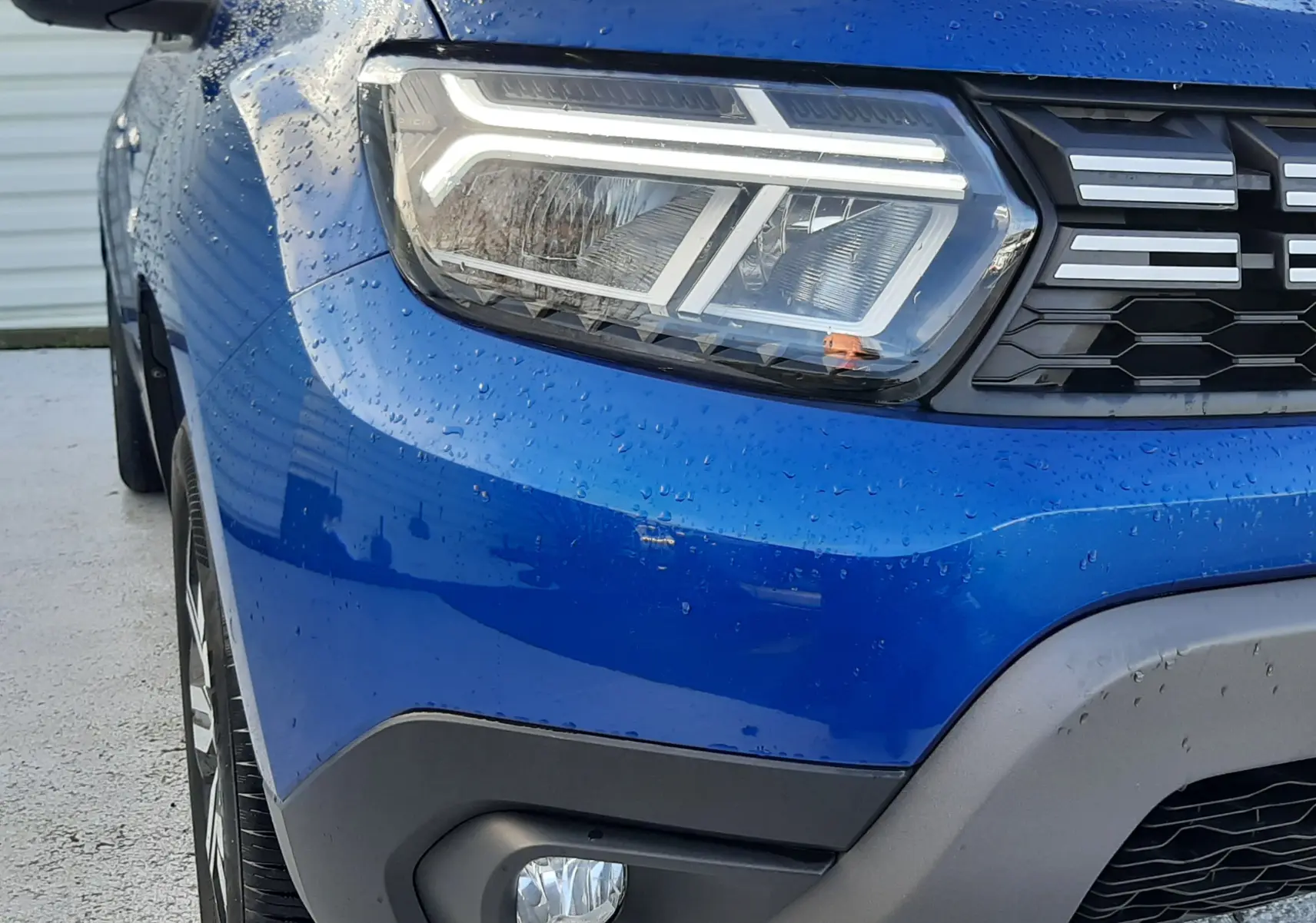 Gros plan sur l'avant gauche du Dacia Duster bleu 2023, mettant en valeur le phare LED et la calandre noire.