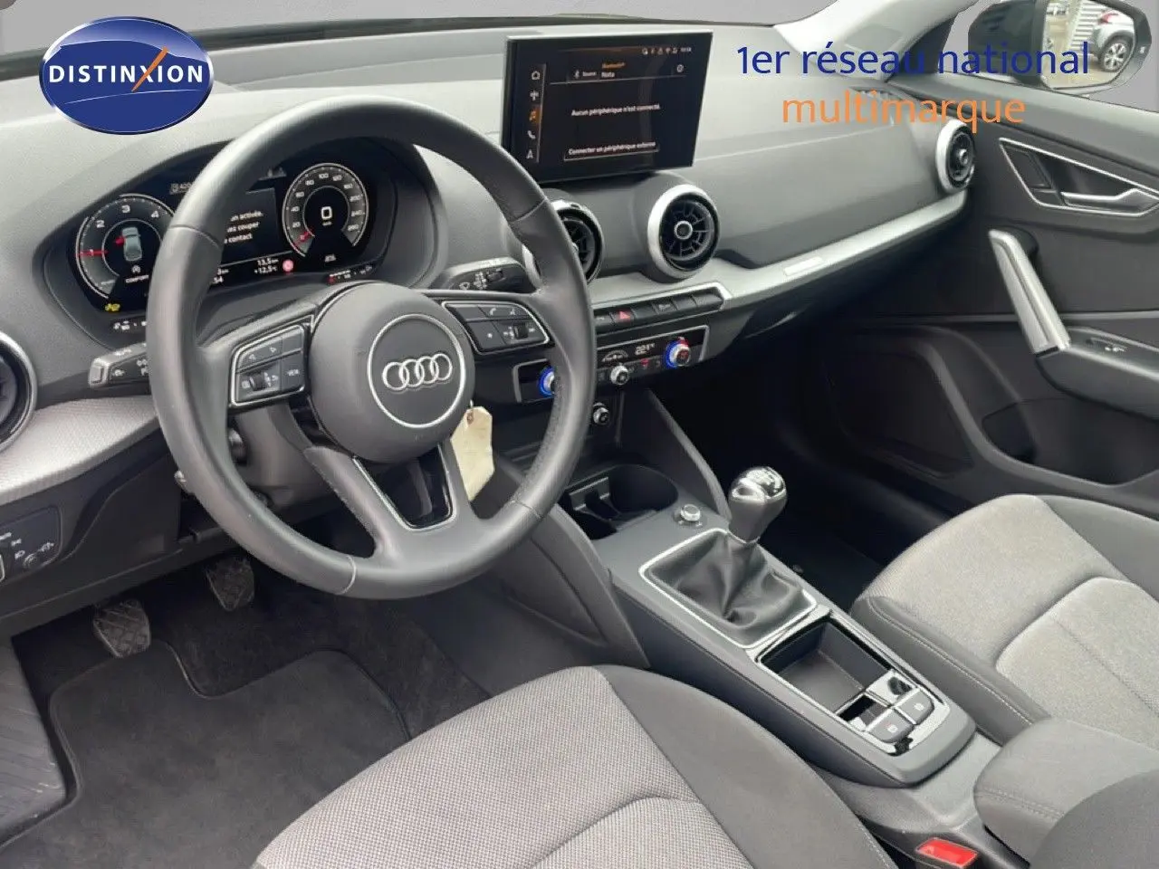 Vue intérieure côté conducteur de l'Audi Q2 30 TDI S-Line 2025, volant cuir, boîte manuelle et tableau de bord digital.