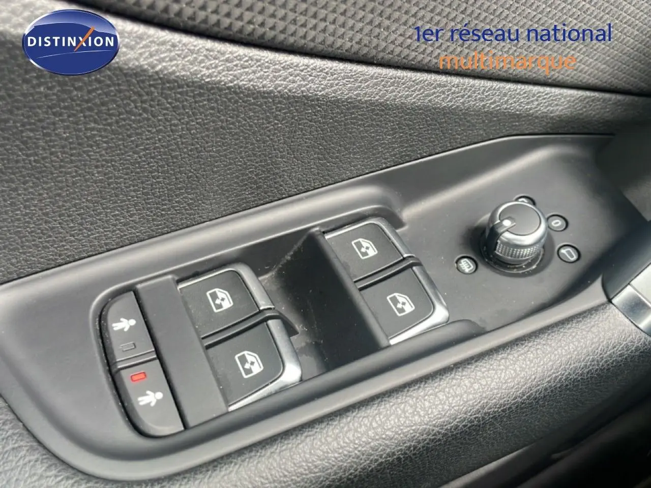 Gros plan sur les commandes de lève-vitres et réglage des rétroviseurs côté conducteur d’un Audi Q2 noir mito metal.