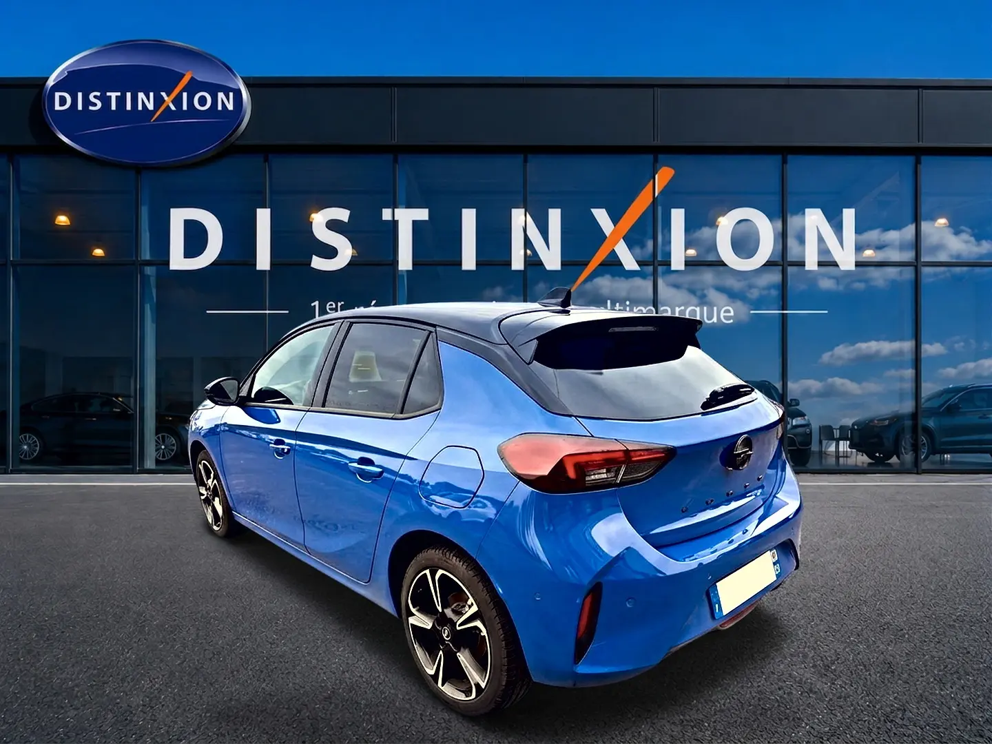 Opel Corsa bleu 3/4 arrière droit avec toit noir et jantes alliage devant showroom Distinxion.
