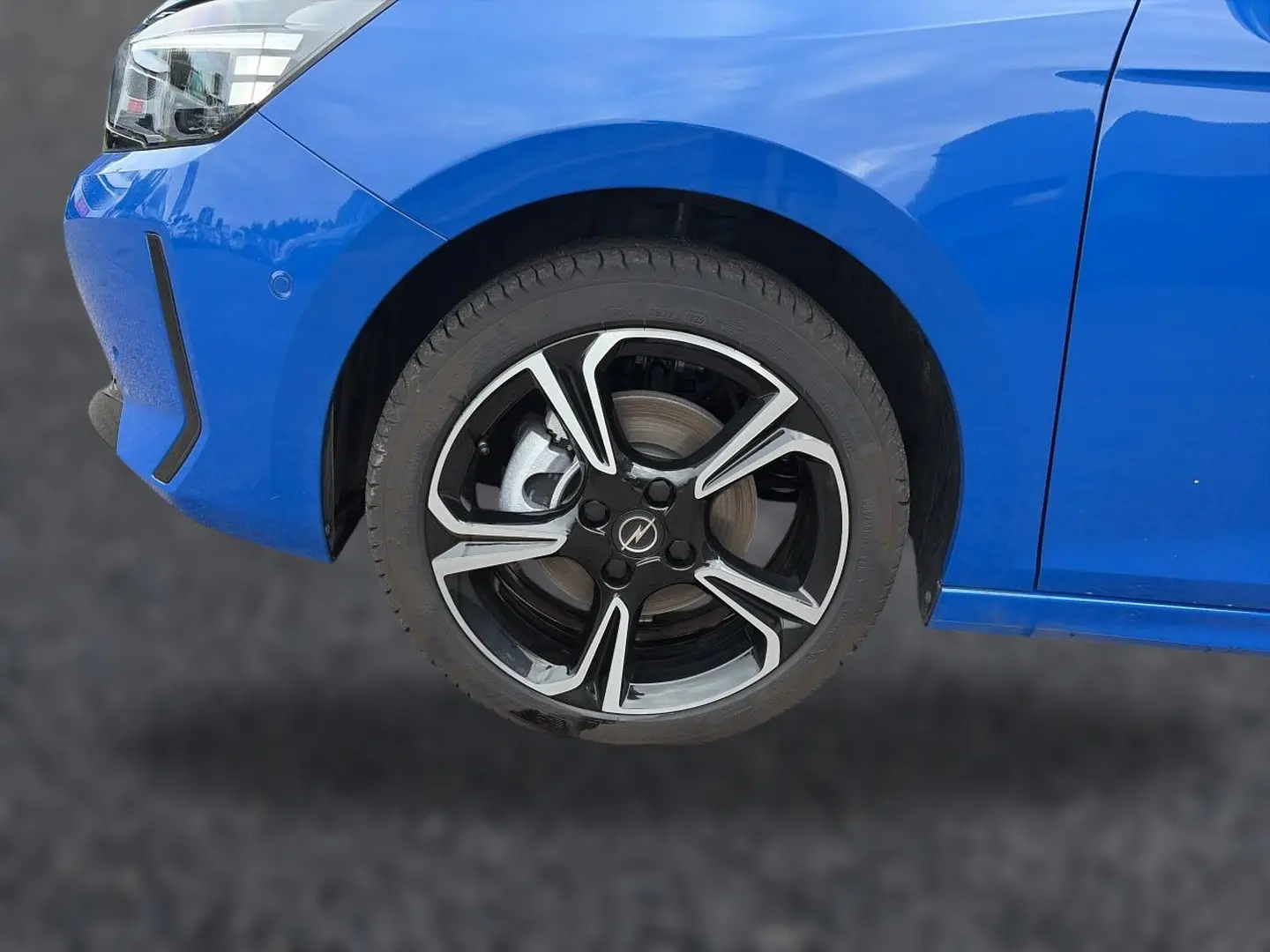 Gros plan sur la roue avant gauche et partie du pare-chocs bleu d'une Opel Corsa 1.2 turbo 100 gs avec jante alu noire et argent.