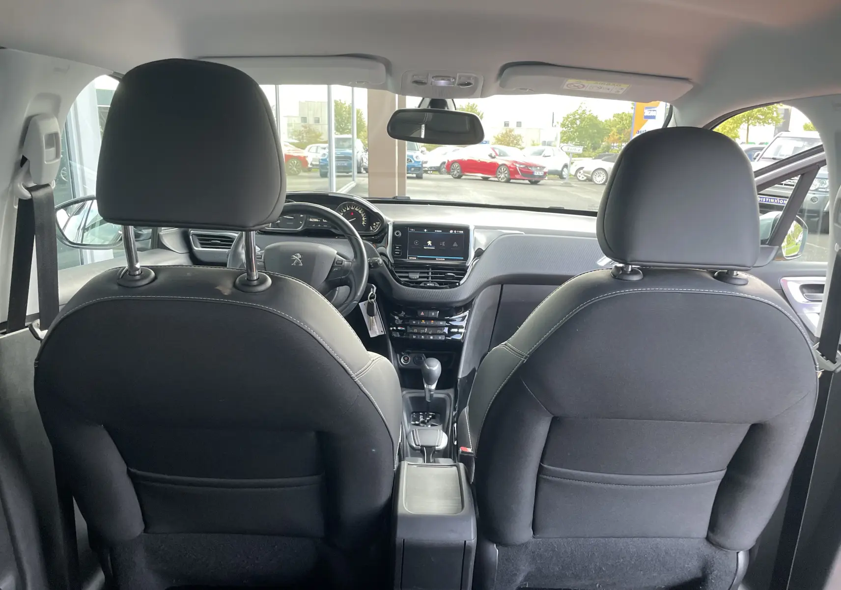 Vue arrière de l'intérieur d'une Peugeot 2008 gris 2019, montrant les sièges avant en tissu noir et le tableau de bord moderne.