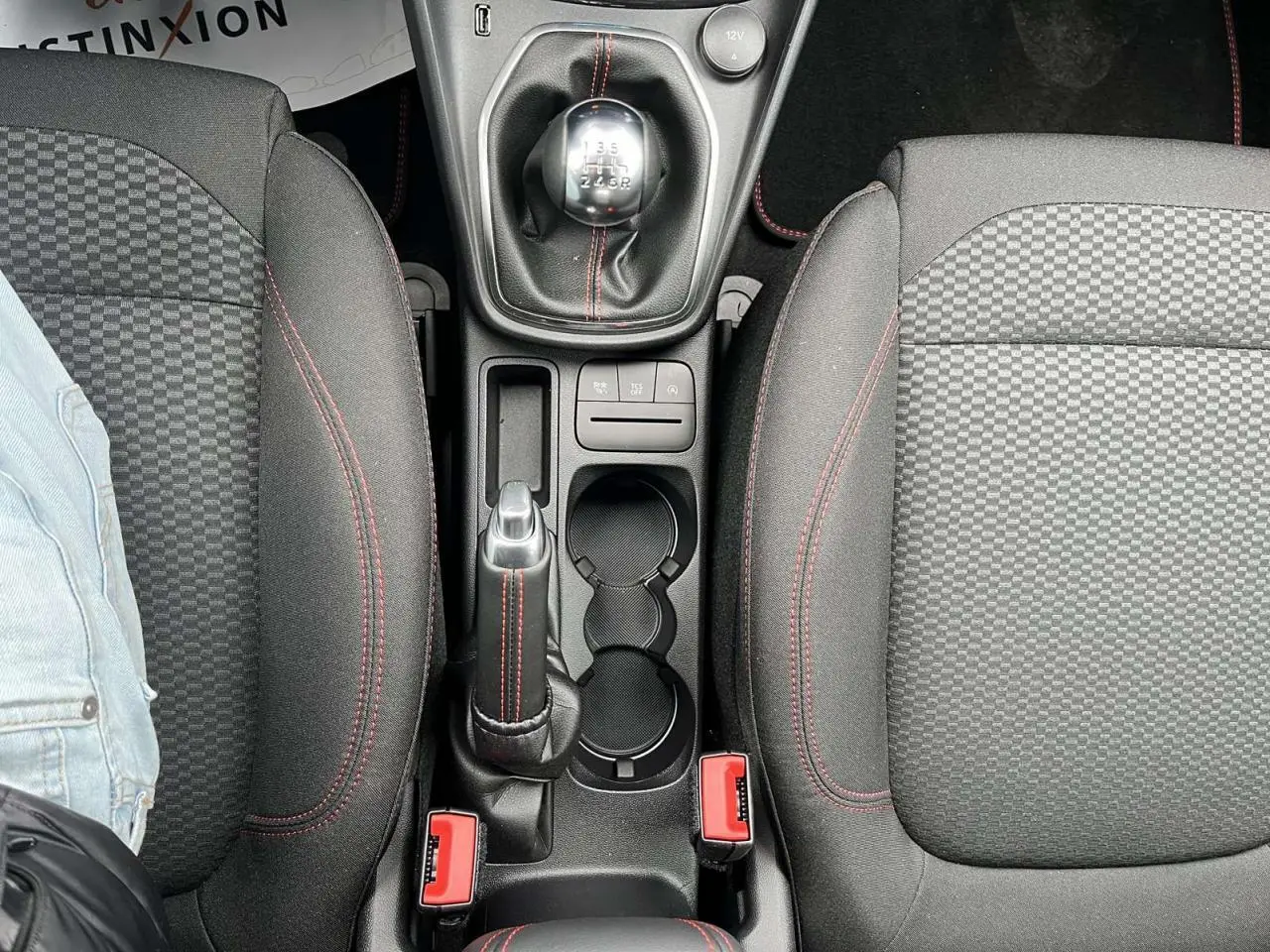 Vue plongeante sur la console centrale du Ford Puma gris Solar, montrant levier de vitesses manuel et sièges noirs à surpiqûres rouges.