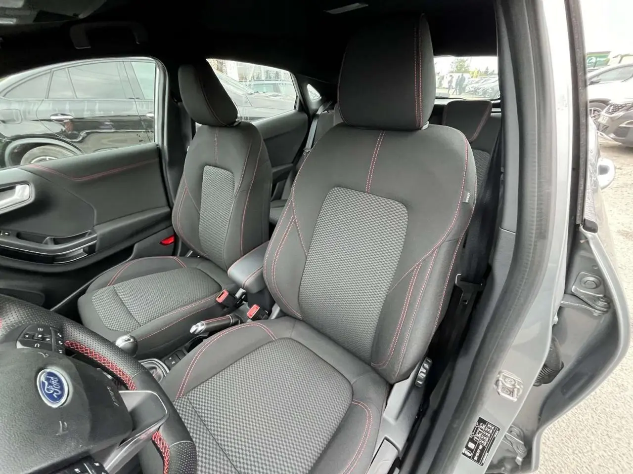 Intérieur avant droit du Ford Puma gris Solar 2023, sièges tissu avec surpiqûres rouges et volant partiellement visible.