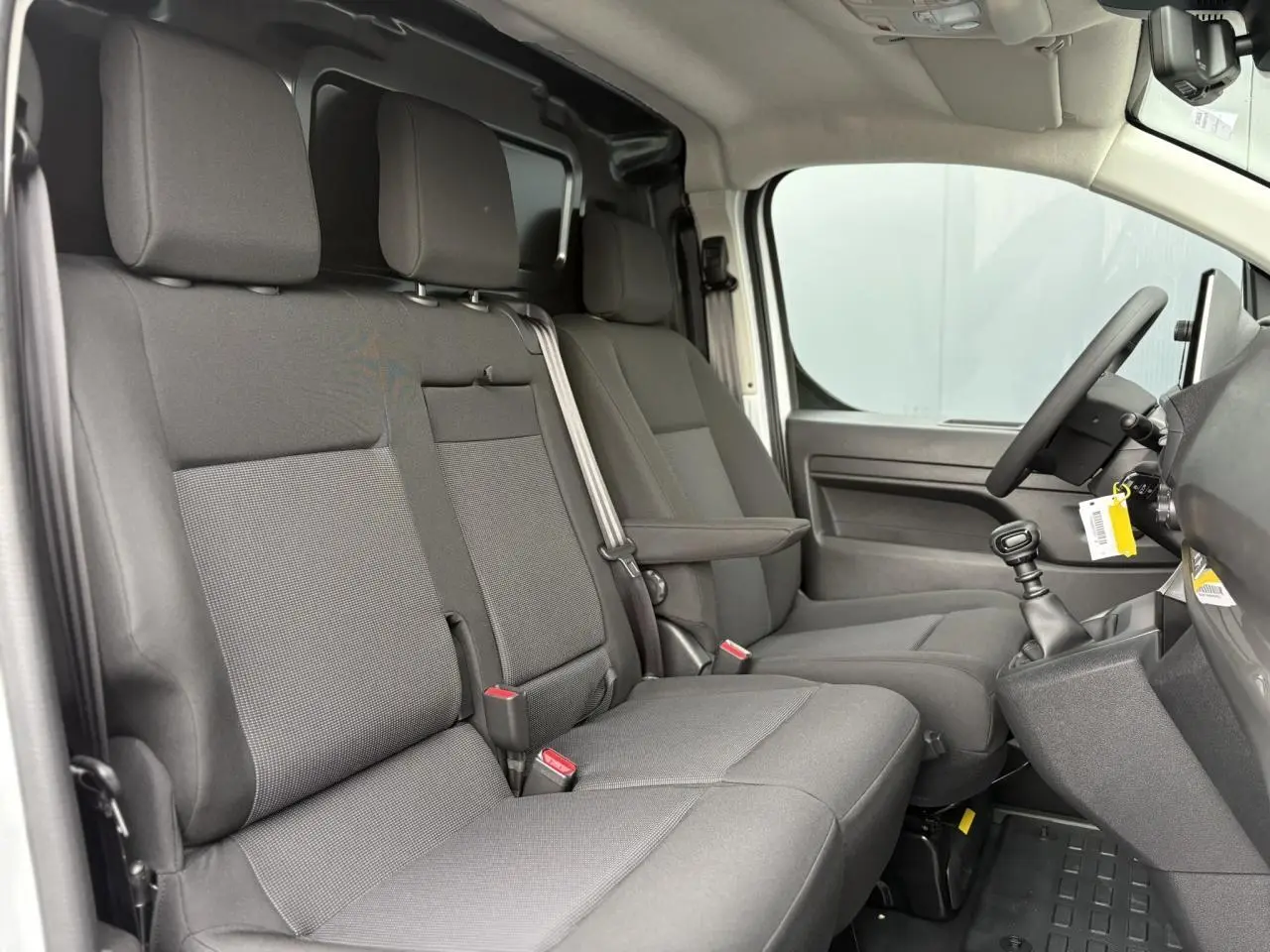 Vue intérieure côté conducteur du Peugeot Expert Fourgon 2025, montrant la banquette passager bi-places en tissu gris et le volant.