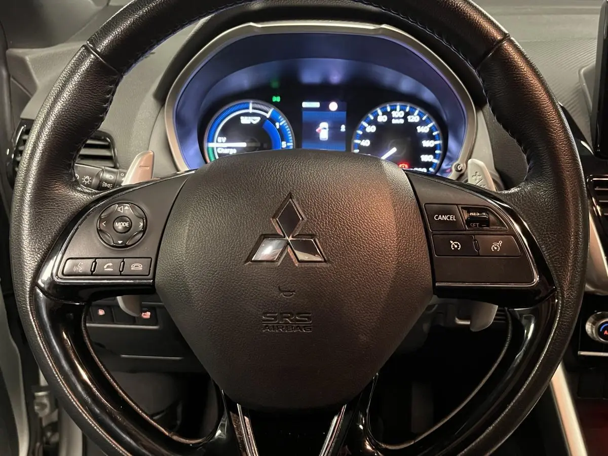 Volant en cuir noir du Mitsubishi Eclipse Cross 2022 avec commandes intégrées et tableau de bord éclairé en arrière-plan.