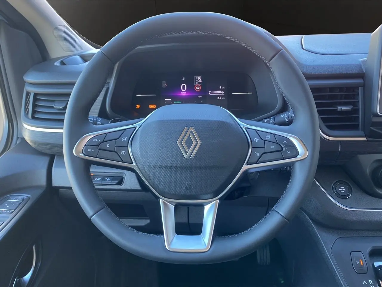 Volant noir en cuir avec logo Renault au centre, tableau de bord digital et bouton start/stop dans un Renault Trafic Combi 2025.